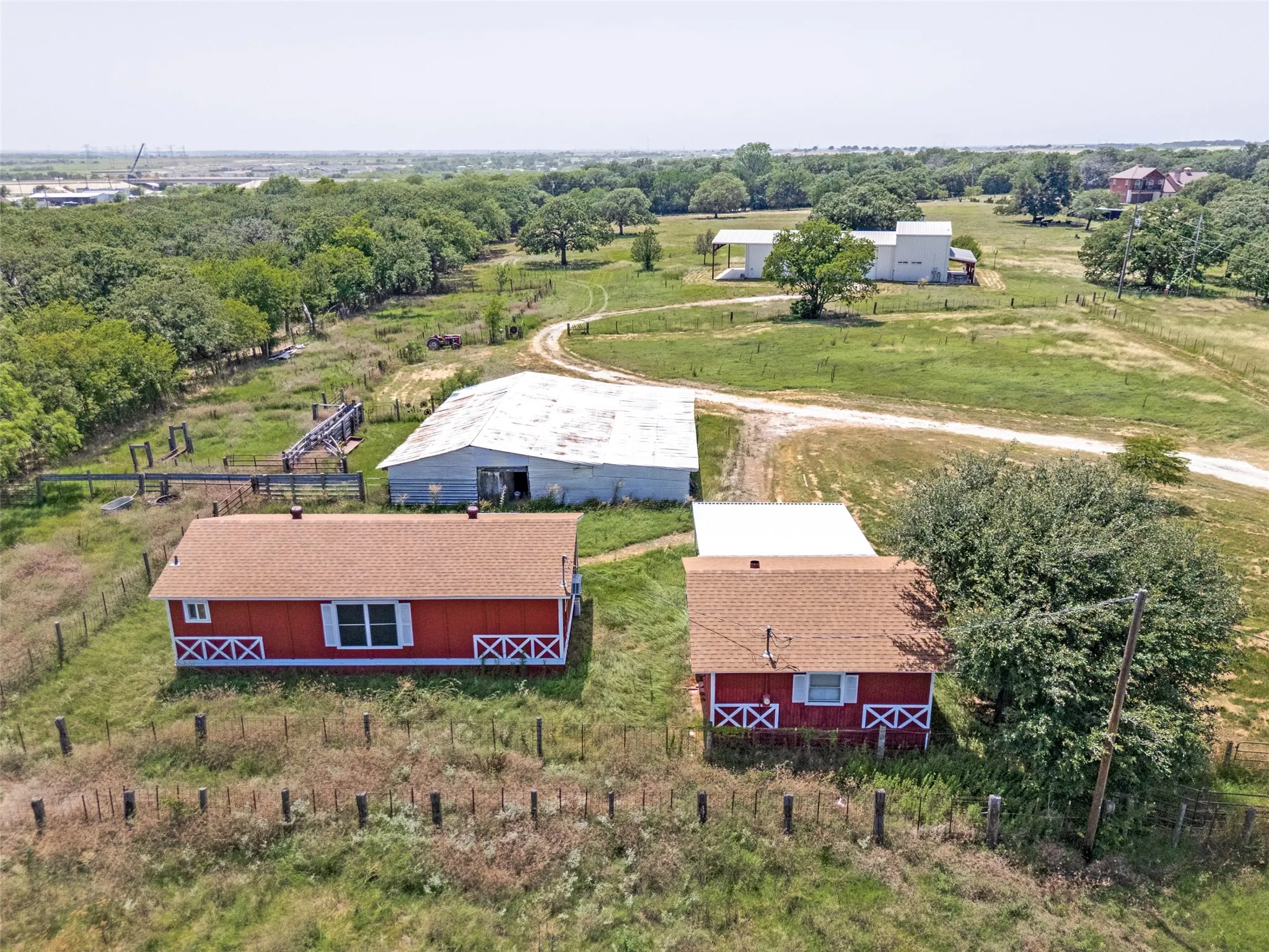 Expansive property featuring multiple structures, including two red-sided buildings with brown shingle roofs, a large white metal-roofed barn, and additional white-sided outbuildings
