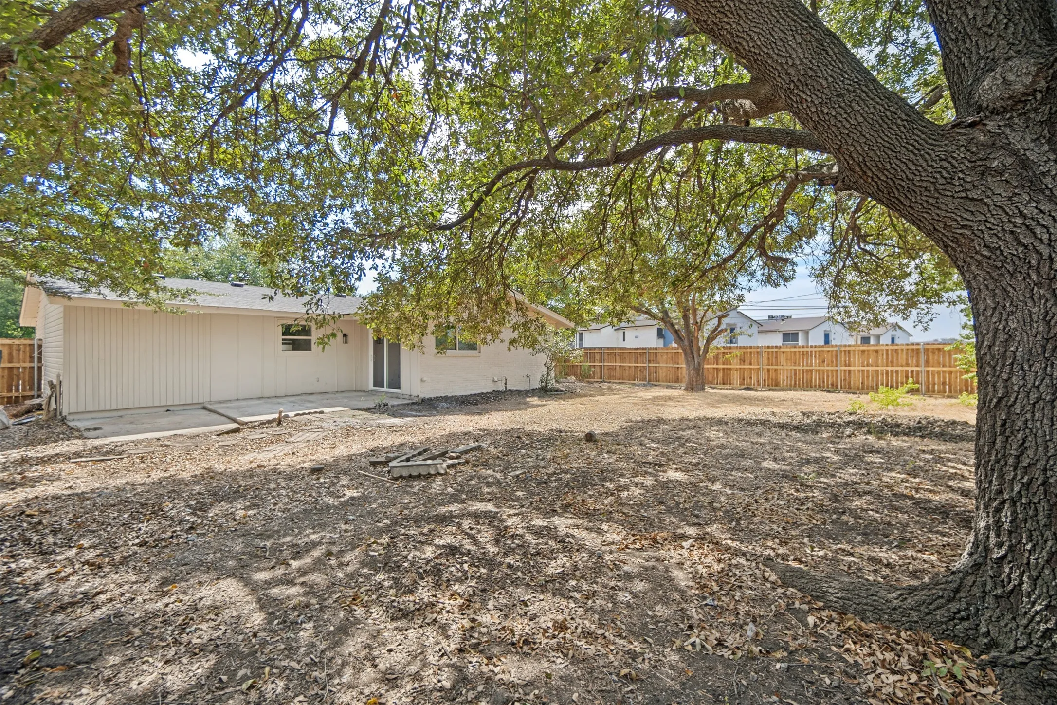 Expansive backyard with mature trees, a concrete patio, and a wood privacy fence