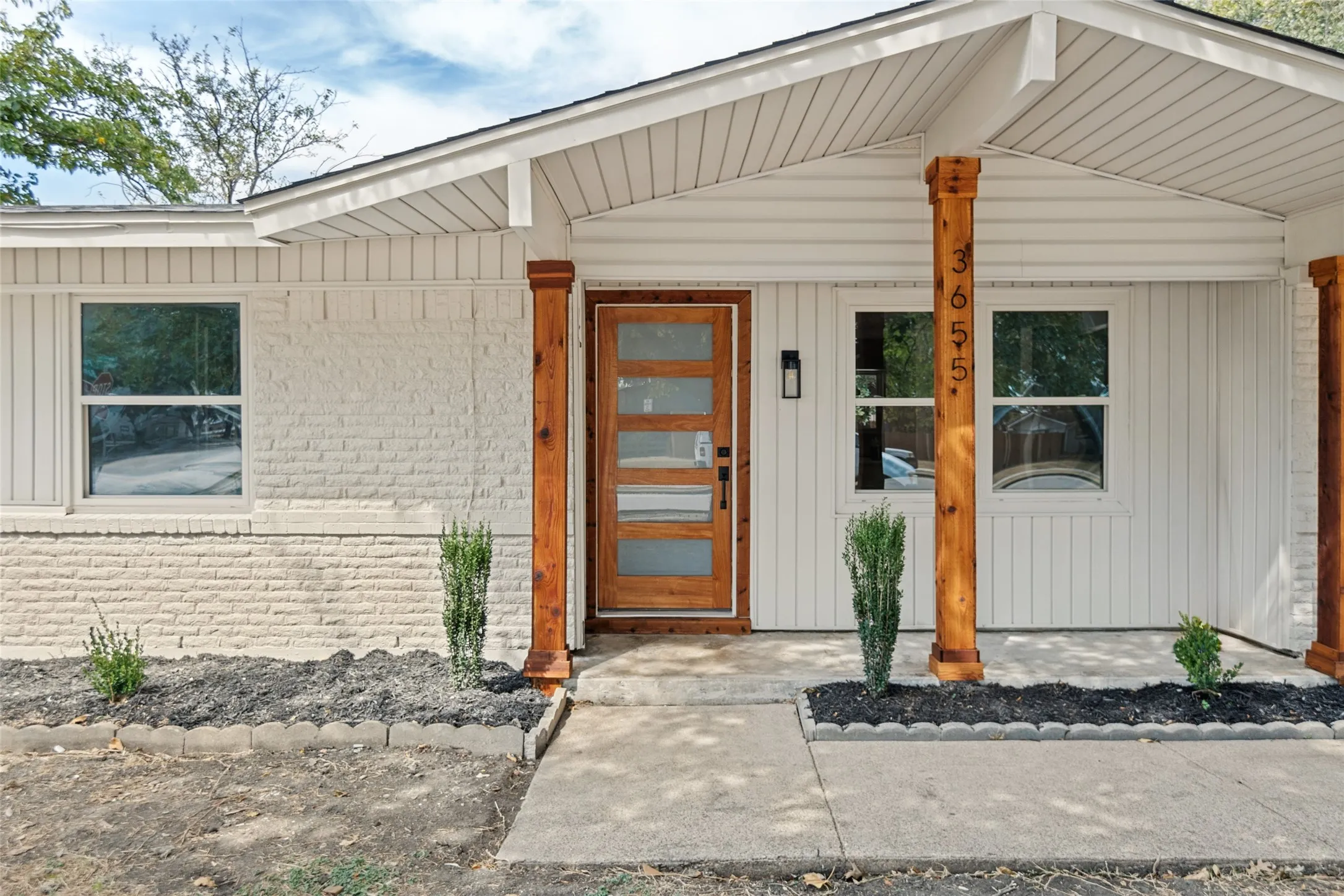White painted brick exterior with vertical white siding, natural wood-finish support columns, a recessed front entry, and a wood-finish door with frosted glass panels