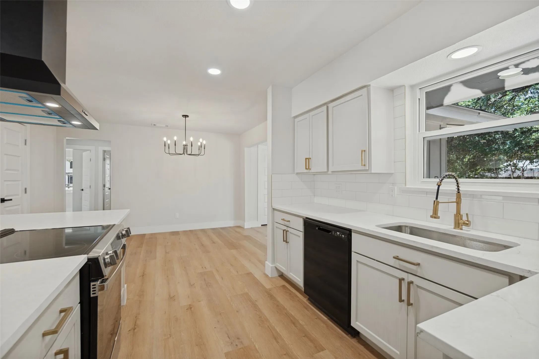 Modern kitchen featuring white cabinetry, light-toned wood-finish flooring, a stainless steel range hood, stainless steel appliances, and recessed lighting