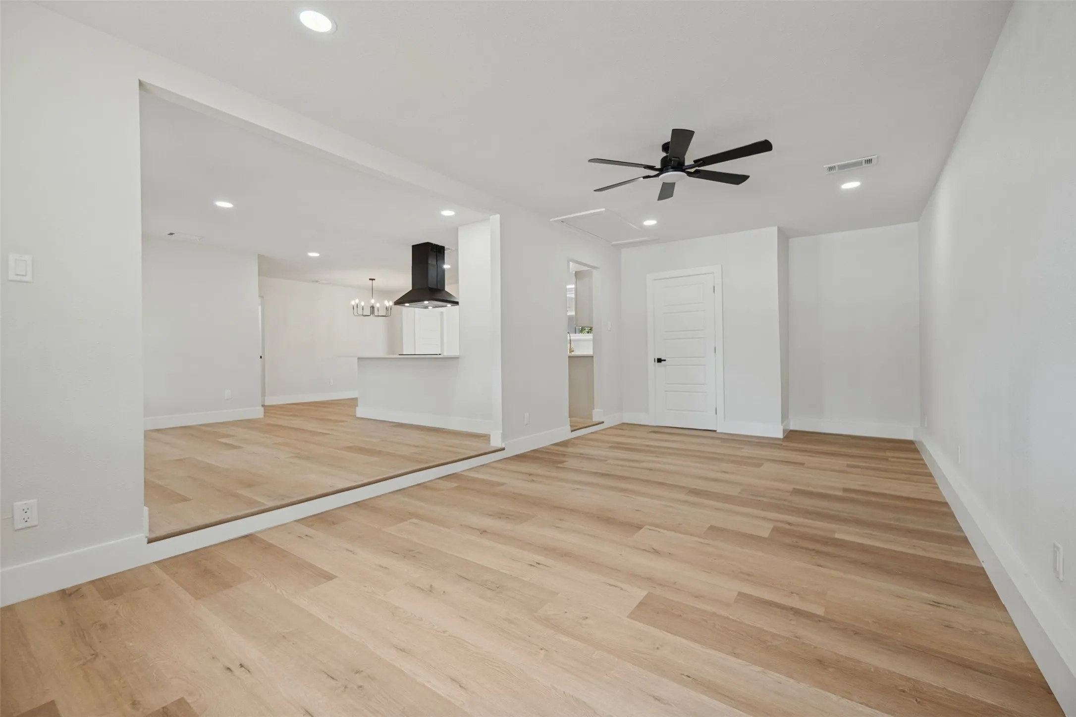 Recessed lighting, wood-finish flooring, ceiling fan, white paneled door, and white baseboards