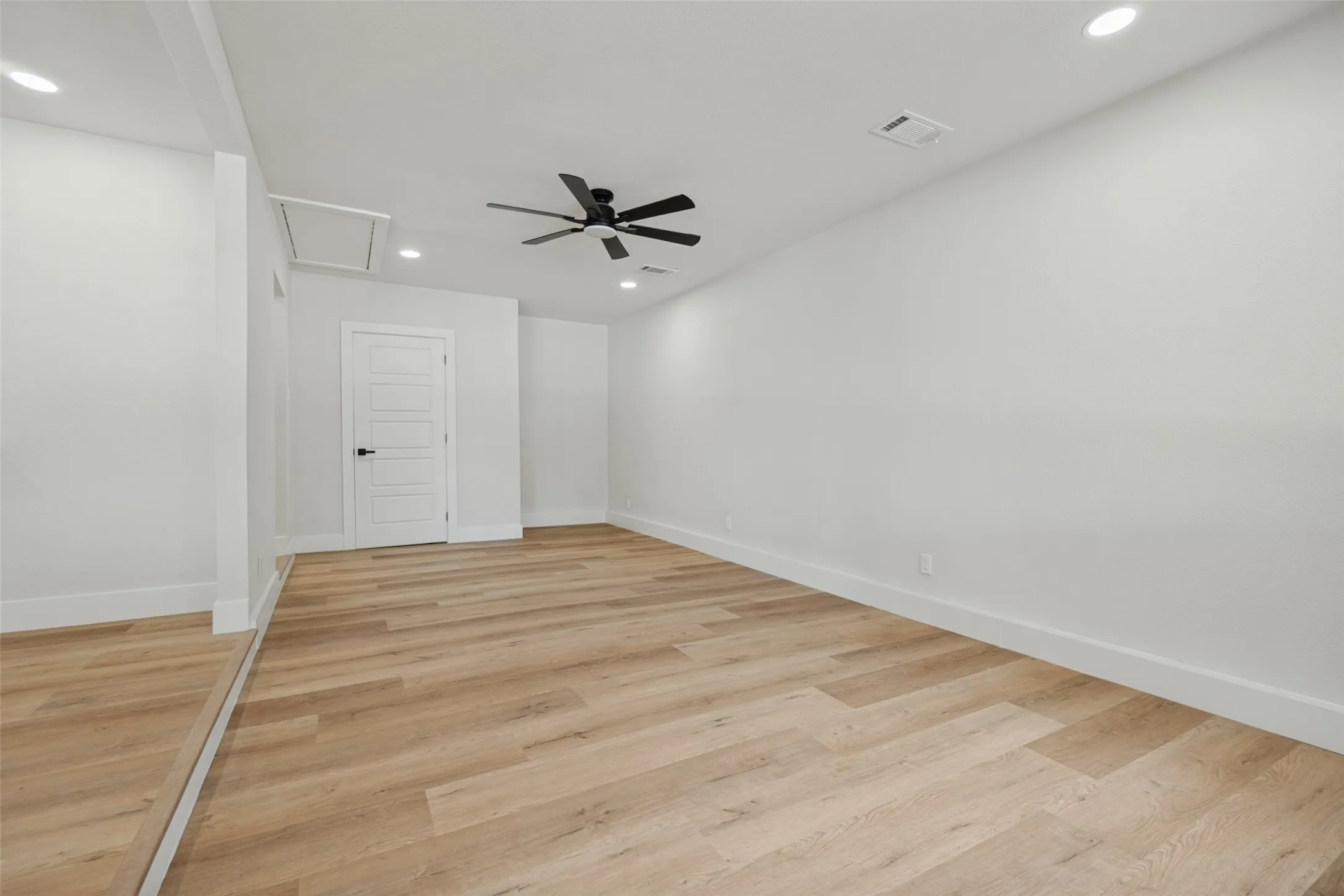 Wood-finish flooring, recessed lighting, ceiling fan, white paneled door with dark hardware, and clean white walls