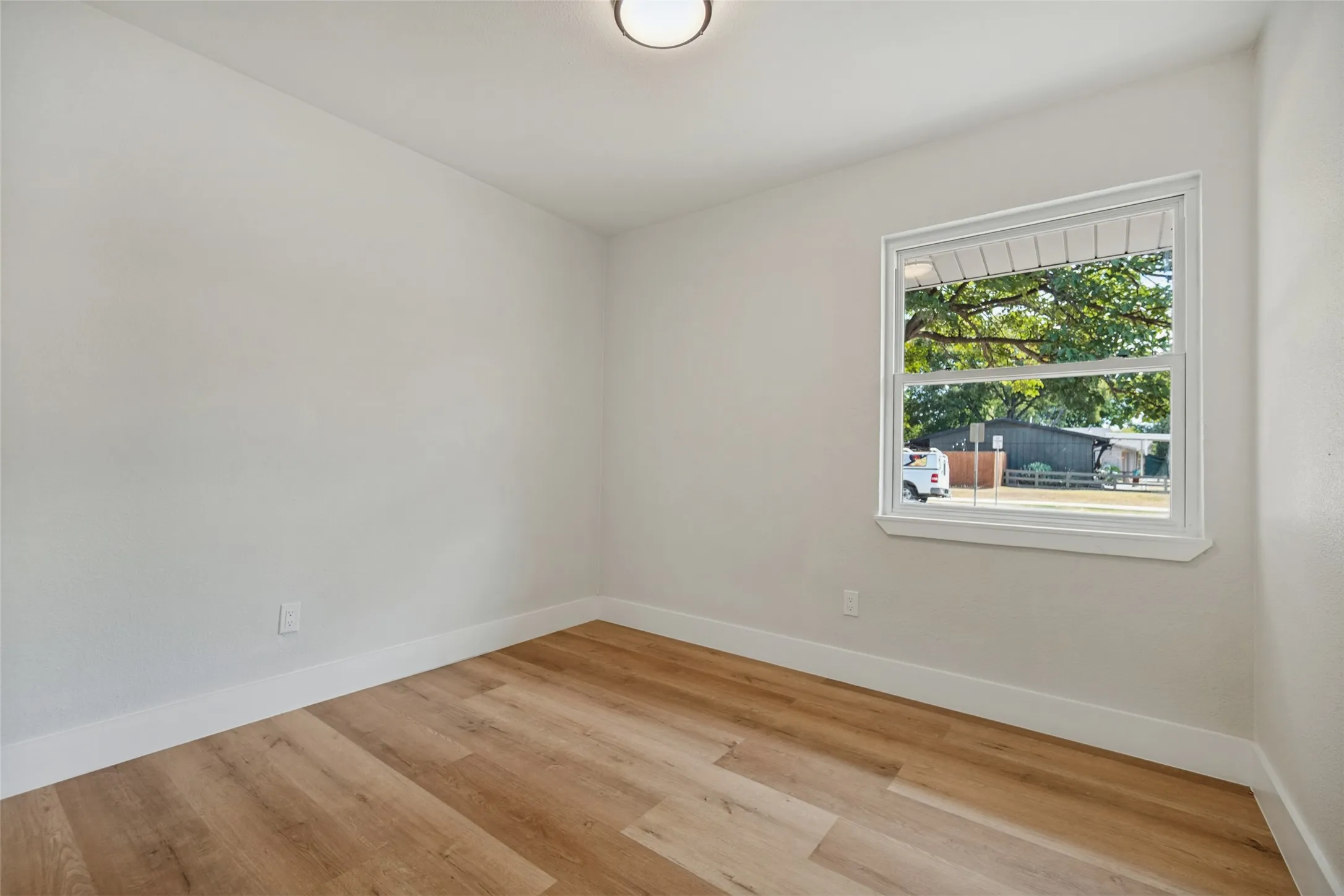 Neutral wall paint, wood-finish flooring, white trim, and a flush-mount ceiling light