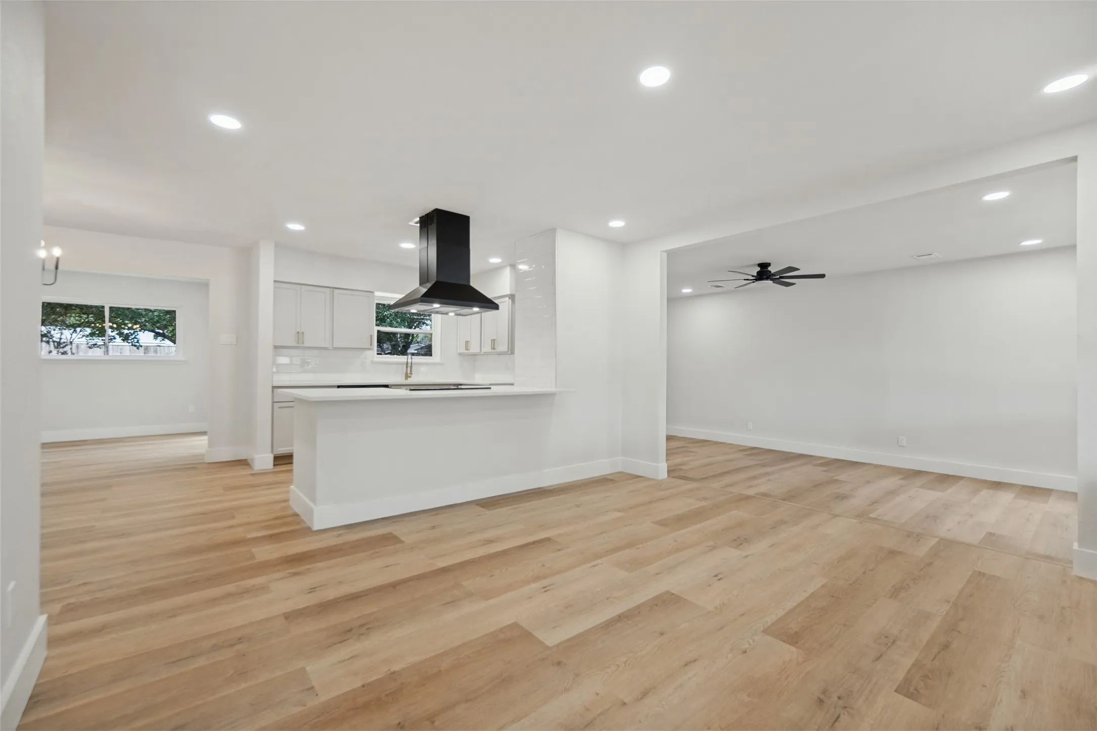 Open concept living space featuring wood-finish flooring, recessed lighting, a kitchen island, and a modern range hood