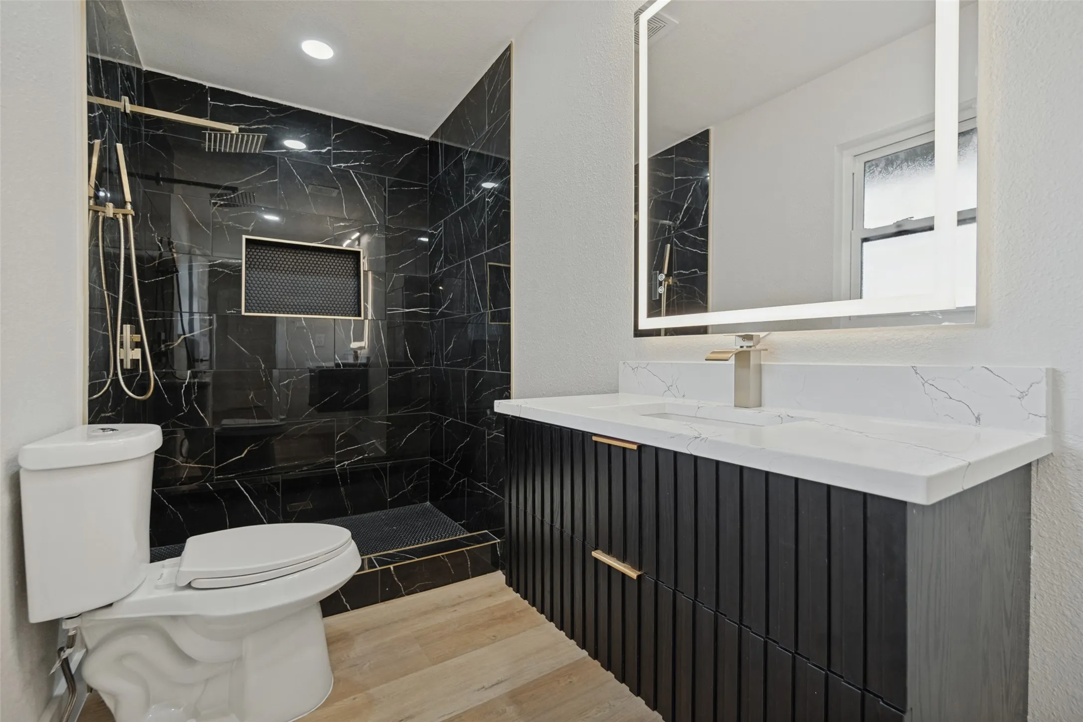 Walk-in shower with black tile surround, gold-finish shower fixtures, and a recessed niche