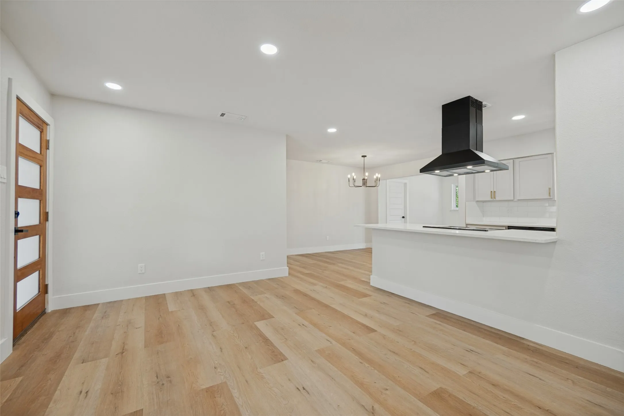 Recessed ceiling lighting, wood-finish flooring, white walls, and a modern black range hood