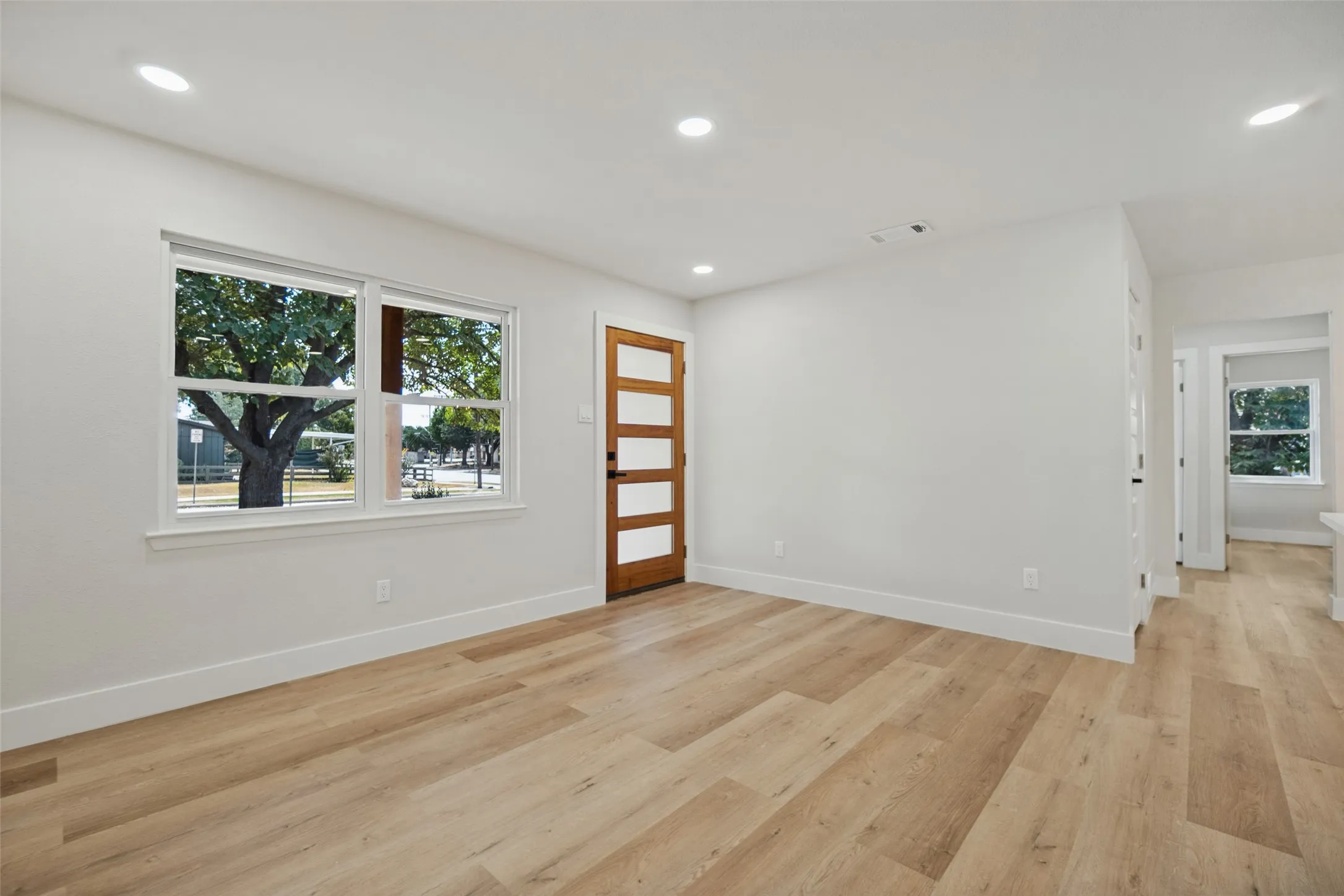 Wood-finish flooring, recessed lighting, white walls, white window trim, and a wood-panel door with frosted glass inserts