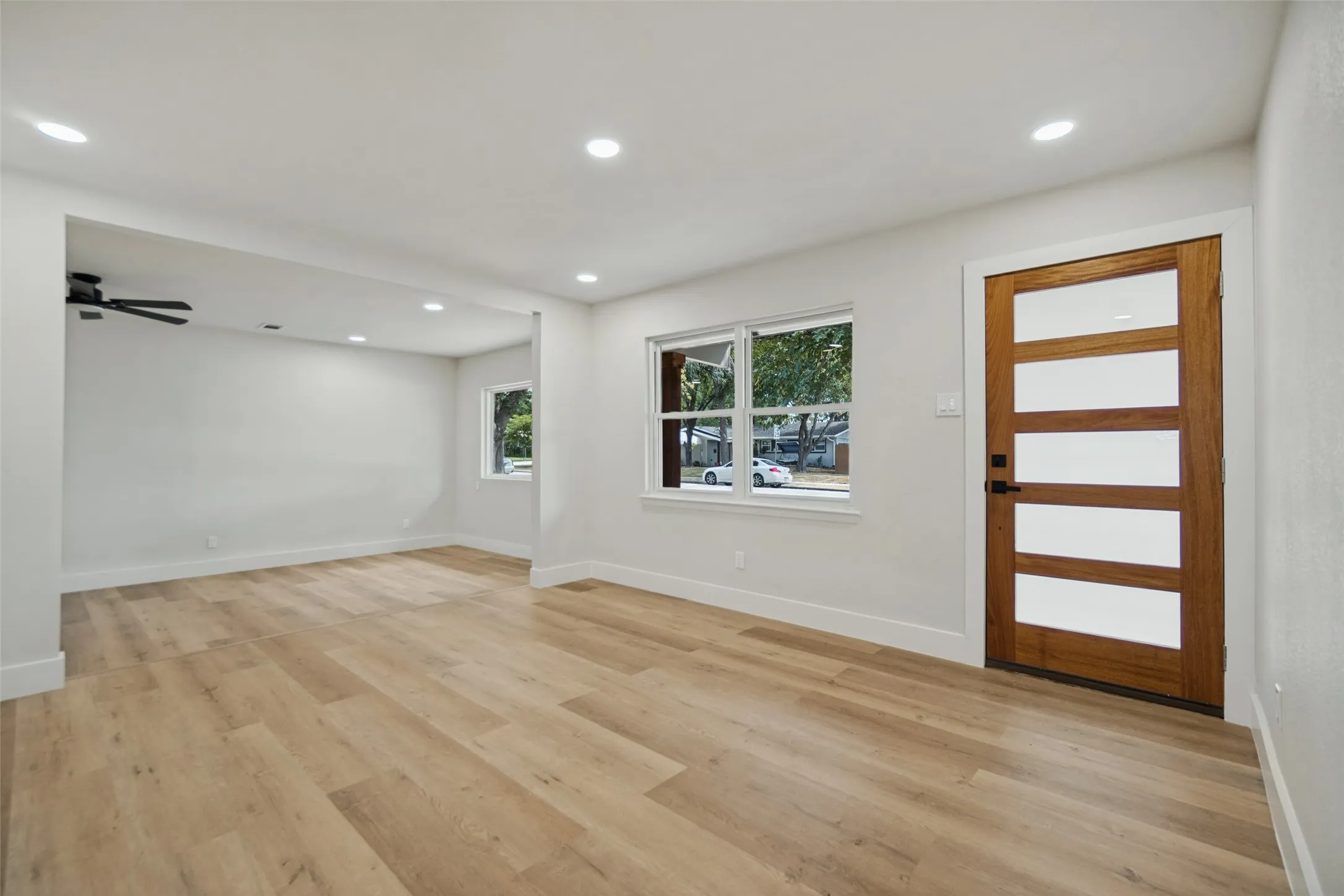 Light wood-finish flooring, recessed lighting, and a modern wood entry door with opaque glass panels