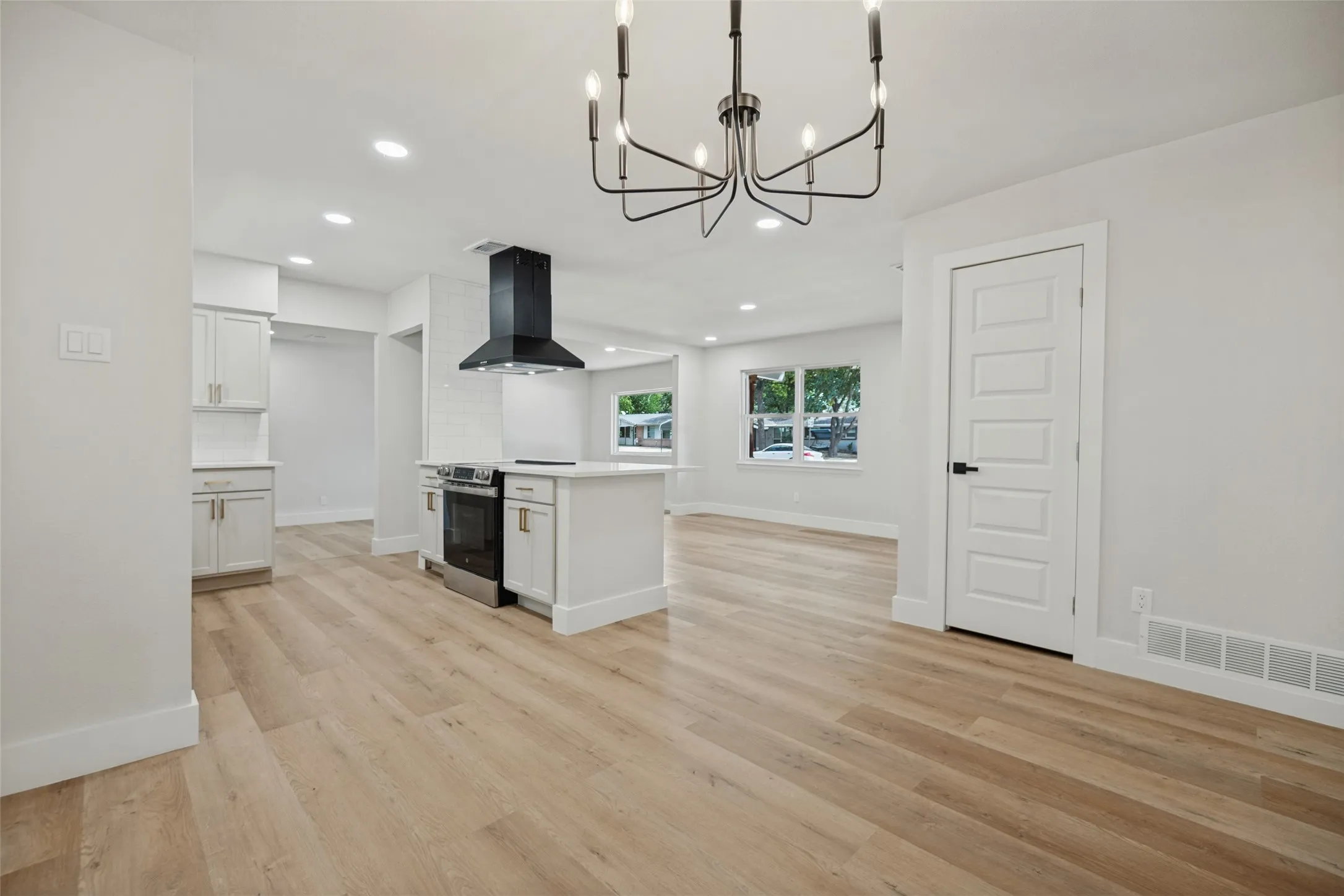 Open-concept living space with wood-finish flooring, white cabinetry, a kitchen island, and a black range hood