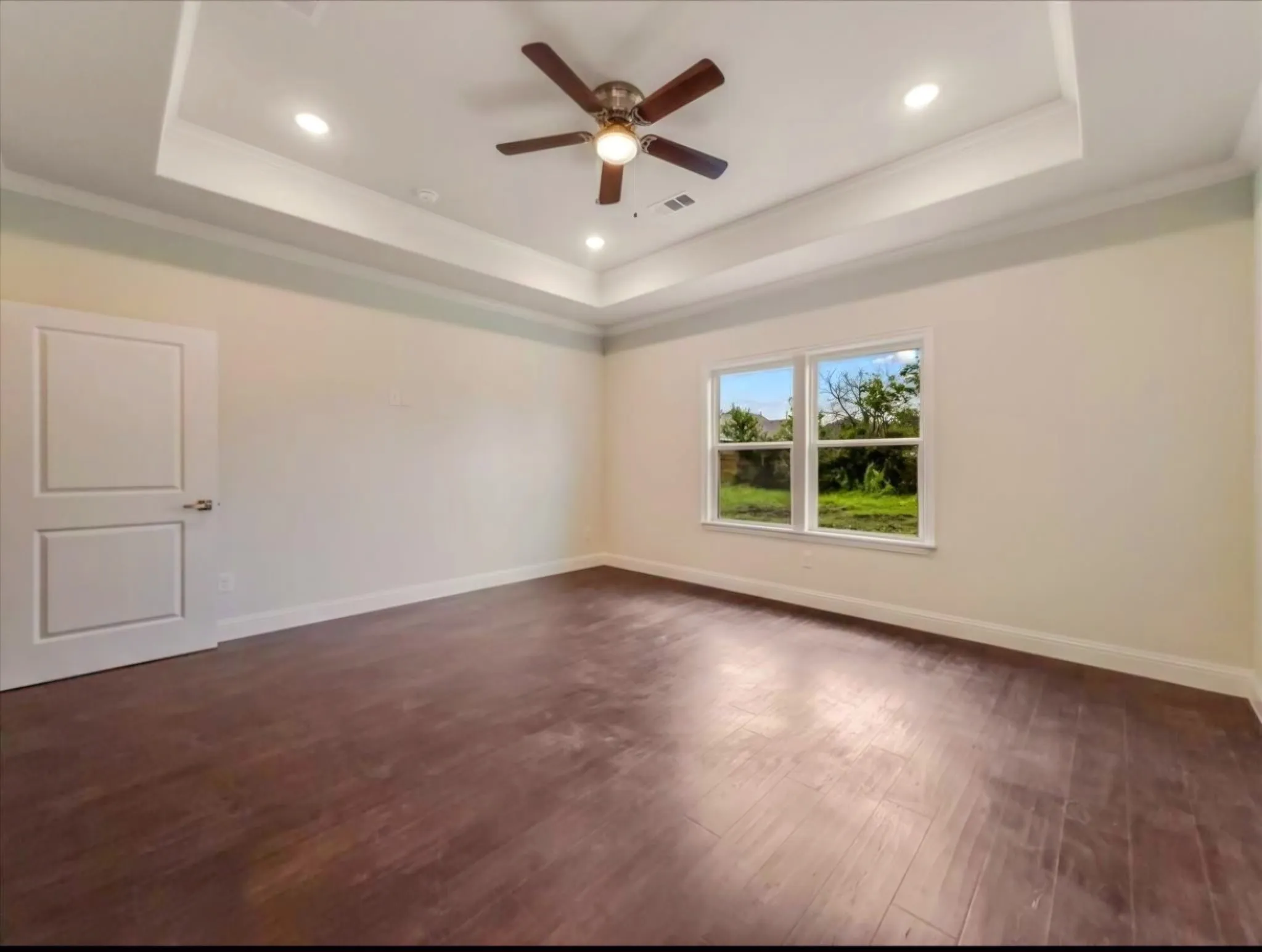 Unfurnished room featuring dark wood-style floors, a ceiling fan, recessed lighting, crown molding, and a raised ceiling