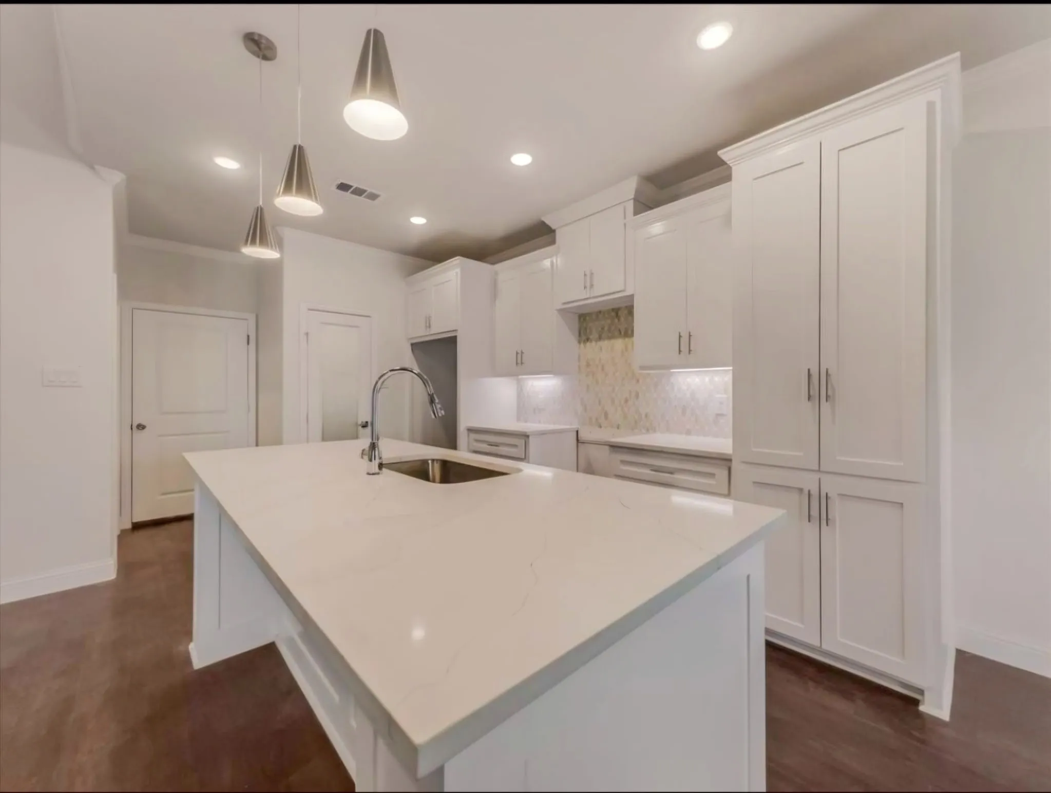 Kitchen featuring light stone countertops, hanging light fixtures, white cabinets, an island with sink, and ornamental molding