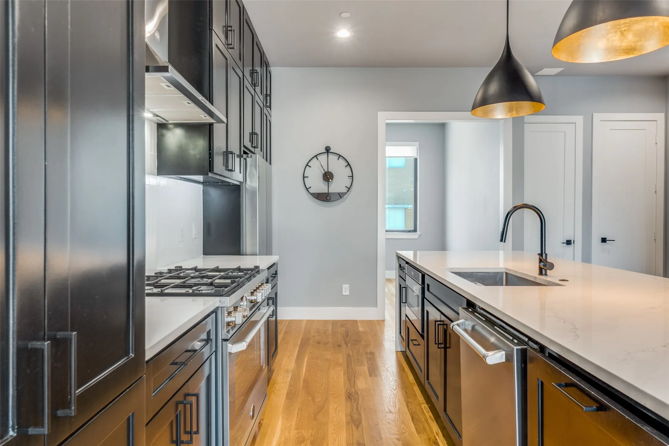 Kitchen featuring dark cabinetry, stainless steel appliances, a center island with sink, pendant lighting, and wood-finish flooring