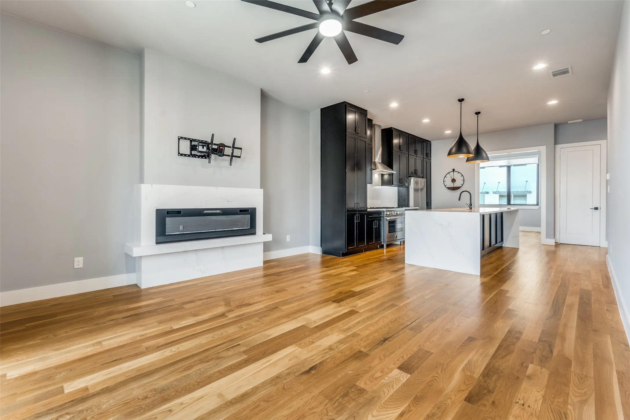 Engineered wood flooring, modern electric fireplace, recessed lighting, black shaker-style cabinetry, and a waterfall island with a sink