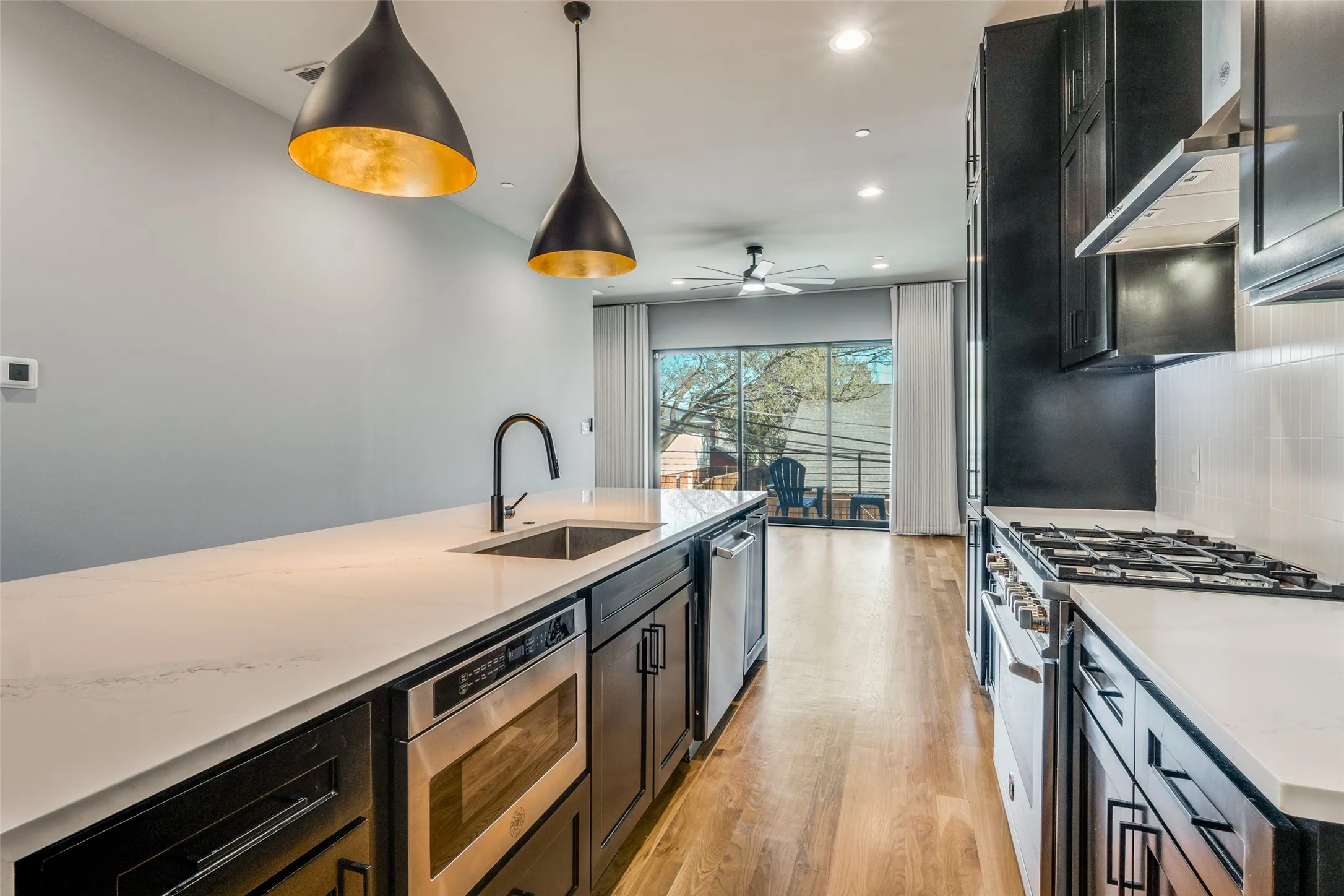 Contemporary kitchen featuring a built-in microwave, stainless steel appliances, wood-finish flooring, and pendant lighting