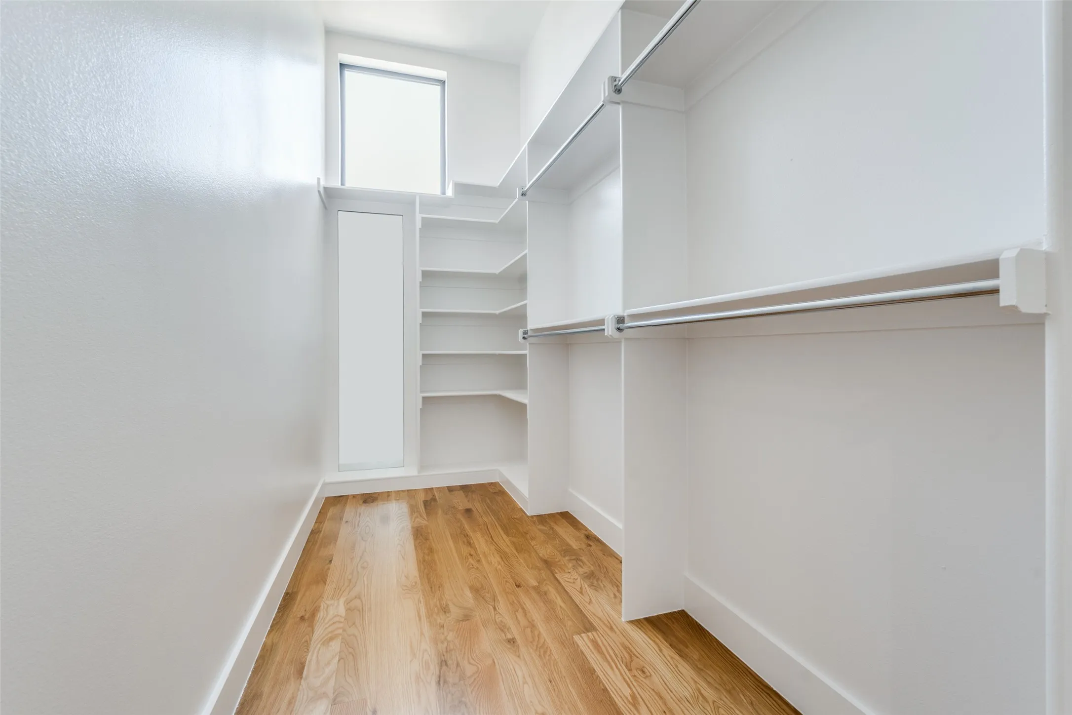 Spacious walk-in closet featuring wood-finish flooring, built-in shelving, and hanging rods