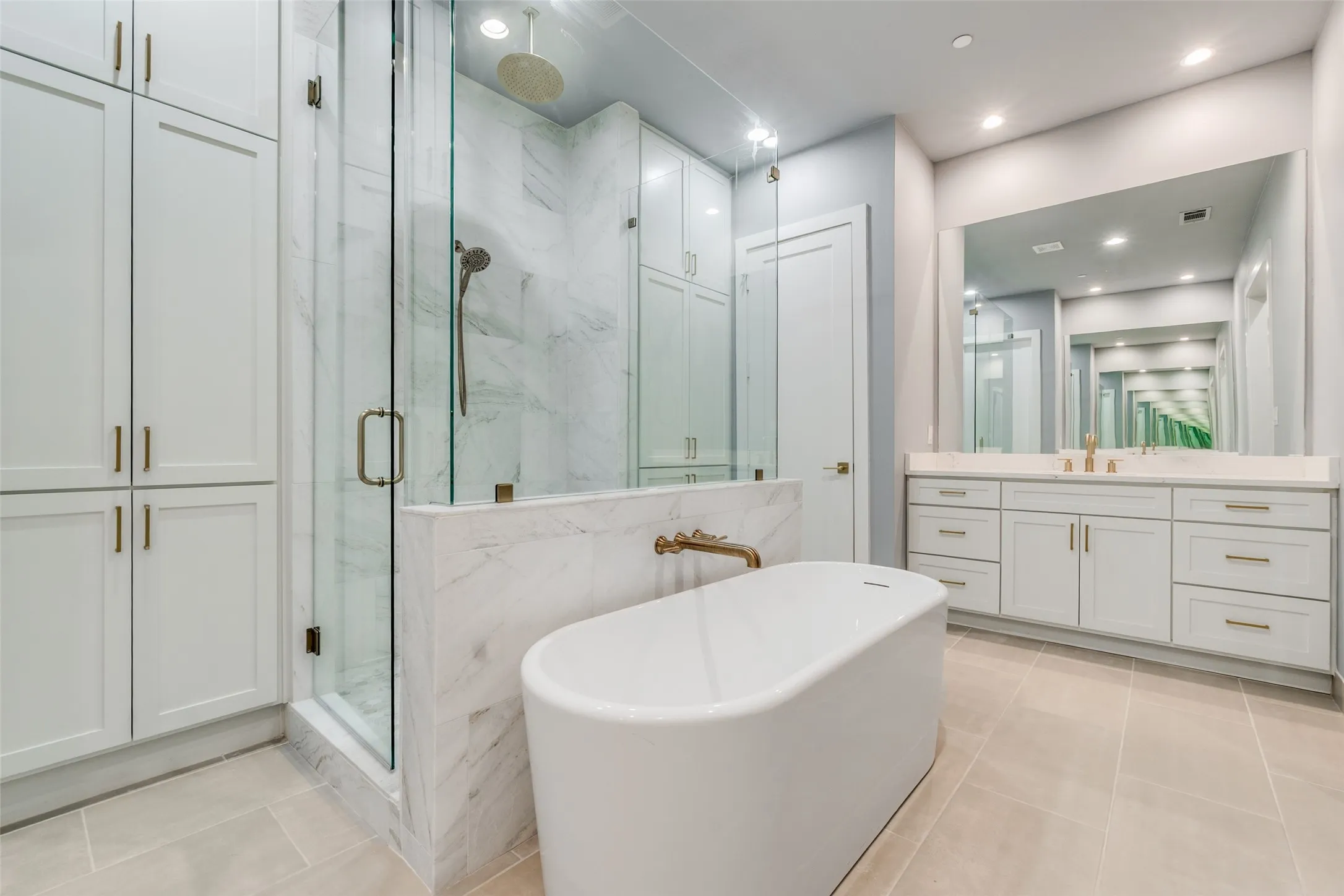 Freestanding soaking tub, glass-enclosed shower with a rain showerhead, double vanity with an integrated mirror, and extensive built-in cabinetry