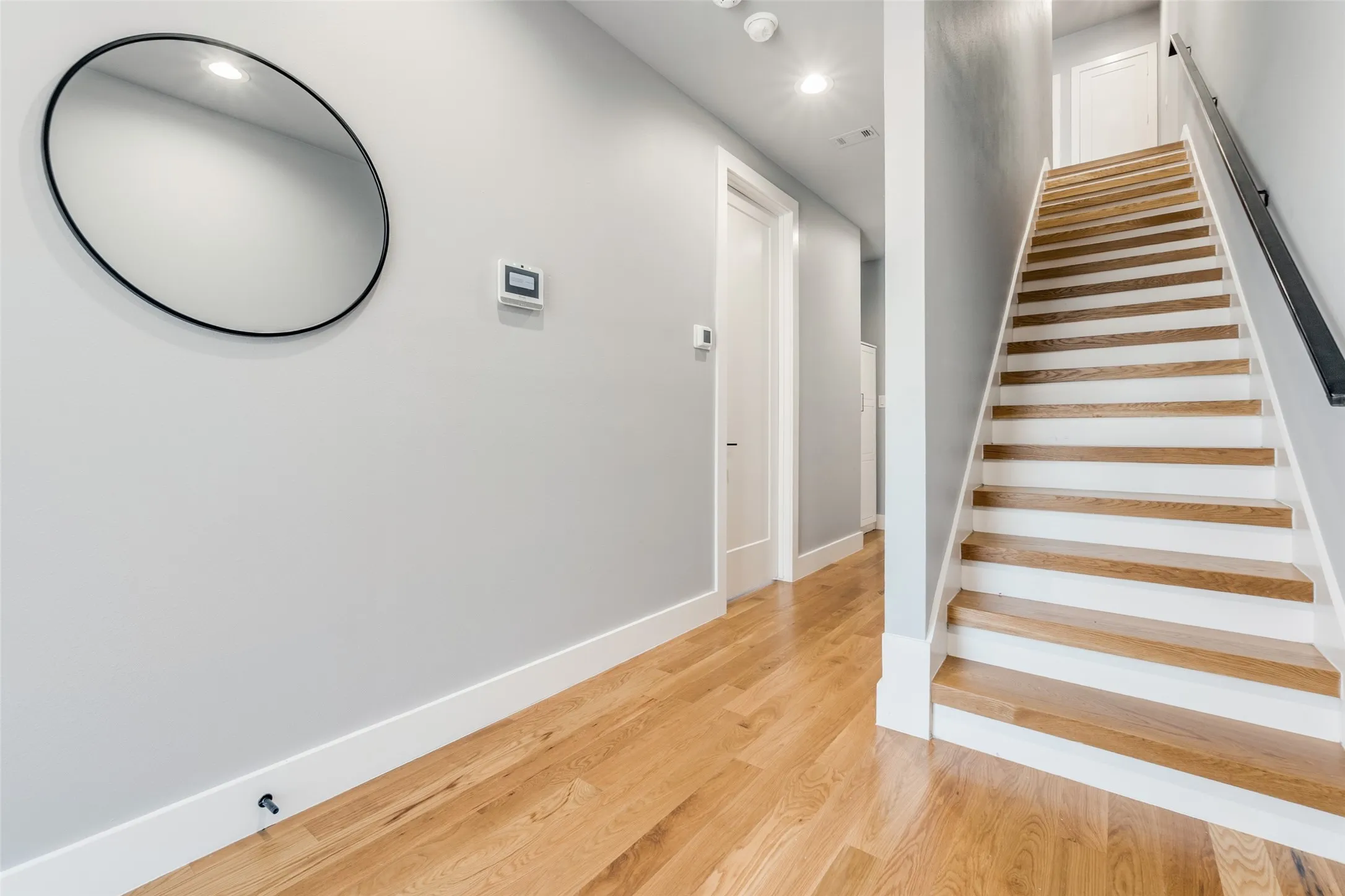 Hardwood flooring, painted walls, white trim, recessed lighting, and a staircase with a dark handrail