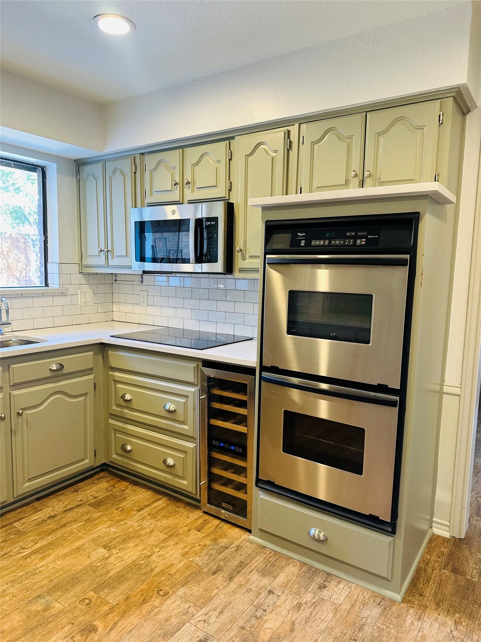 Kitchen featuring light-toned cabinetry, stainless steel appliances, white subway tile backsplash, light countertops, and wood-finish flooring