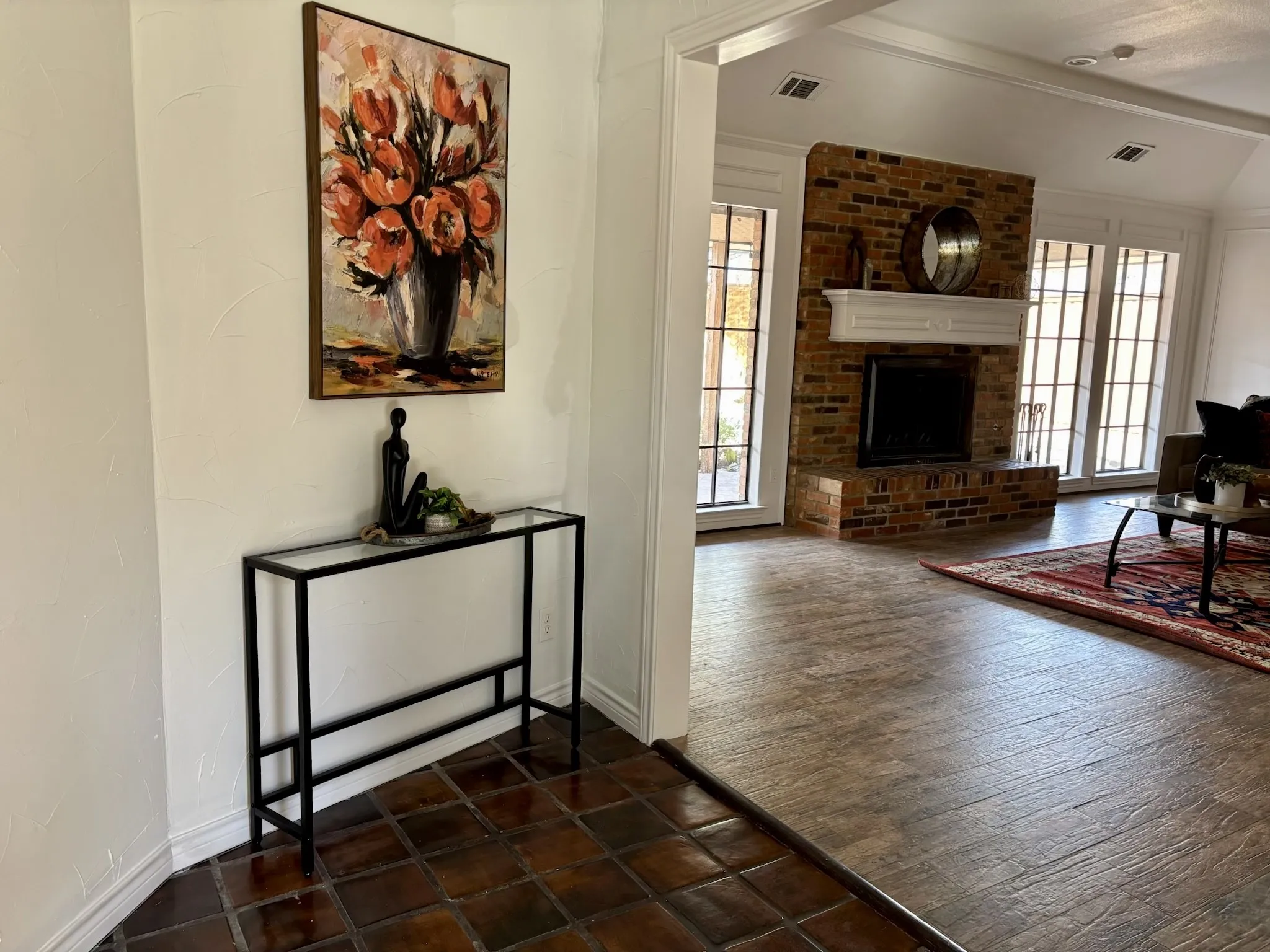 Brick fireplace with a white mantel, wood-finish flooring, and multiple glass-paned windows