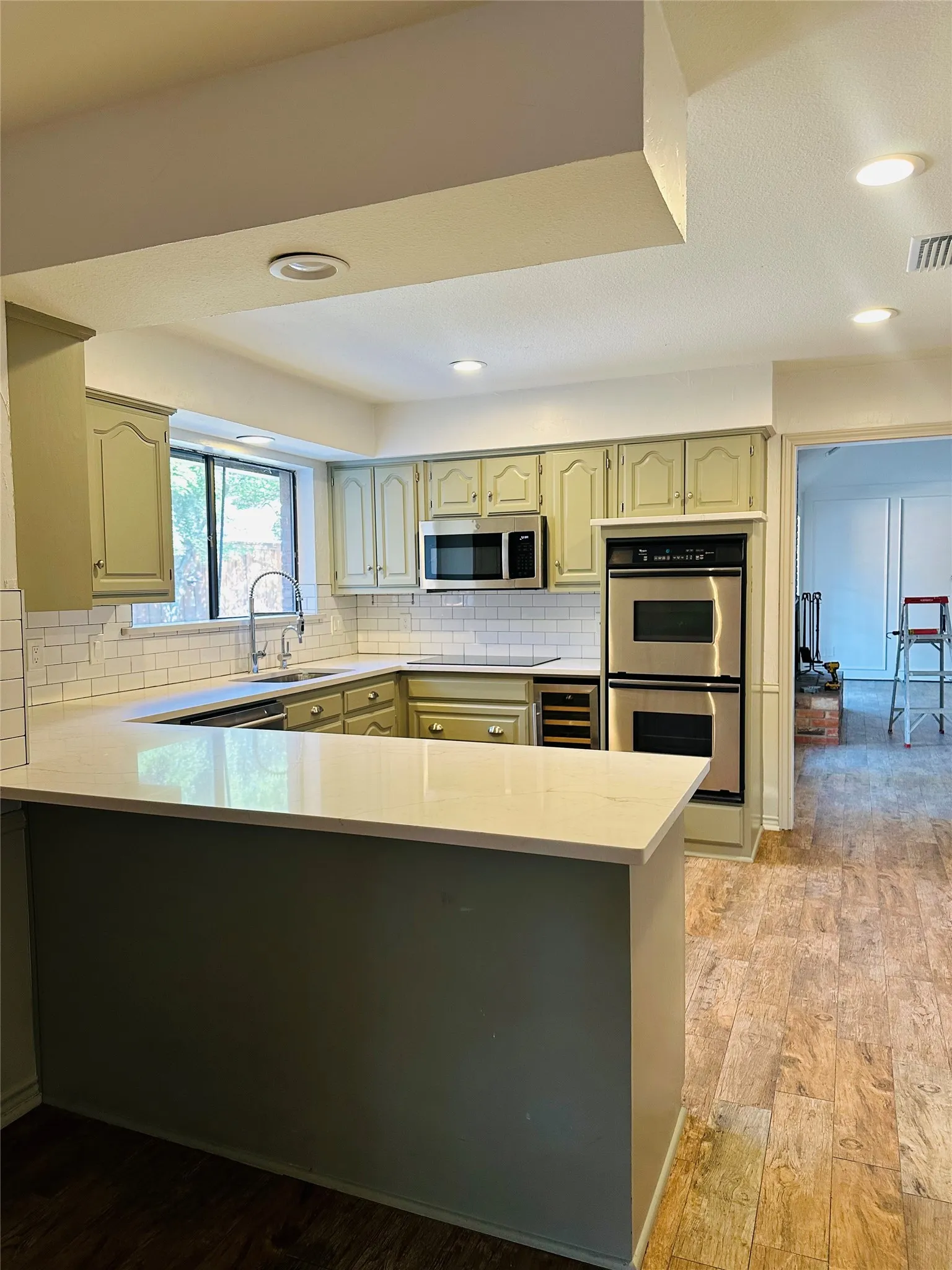 U-shaped kitchen with light green cabinetry, white subway tile backsplash, stainless steel appliances, and wood-finish flooring