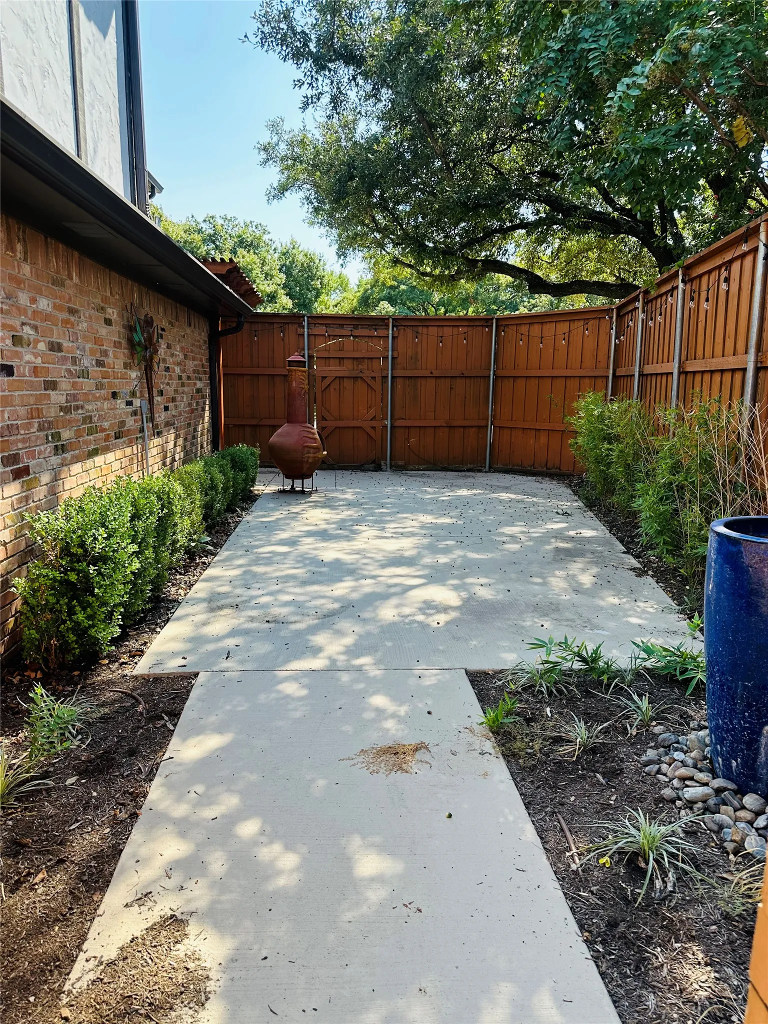 Patio area featuring concrete paving, brick exterior wall, wood fencing, and established perimeter landscaping