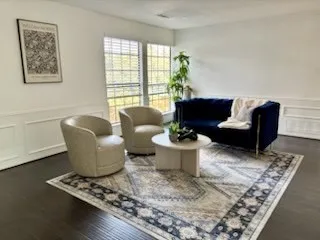 Dark wood-finish flooring, white wall paneling, and multiple windows with blinds