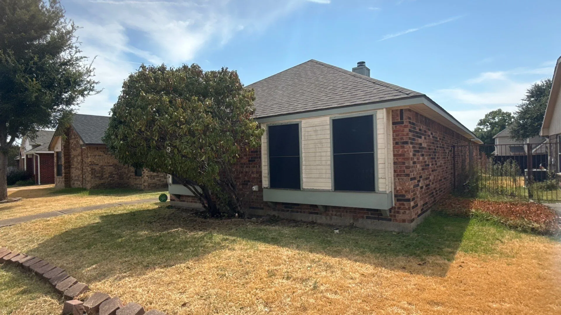 Brick exterior with a shingled roof, a mature front yard tree, and an established lawn