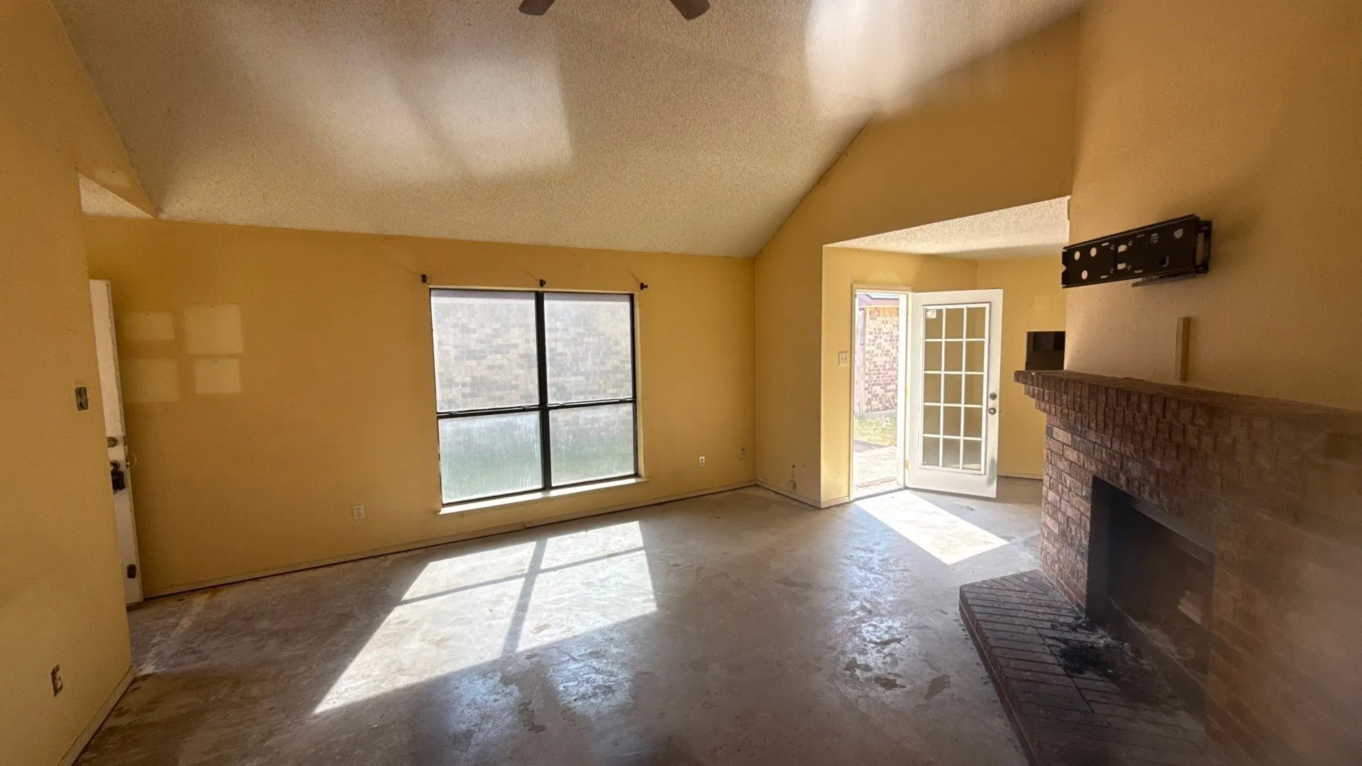 Vaulted ceiling, brick fireplace, dual-pane window, and a glass-paneled exterior door