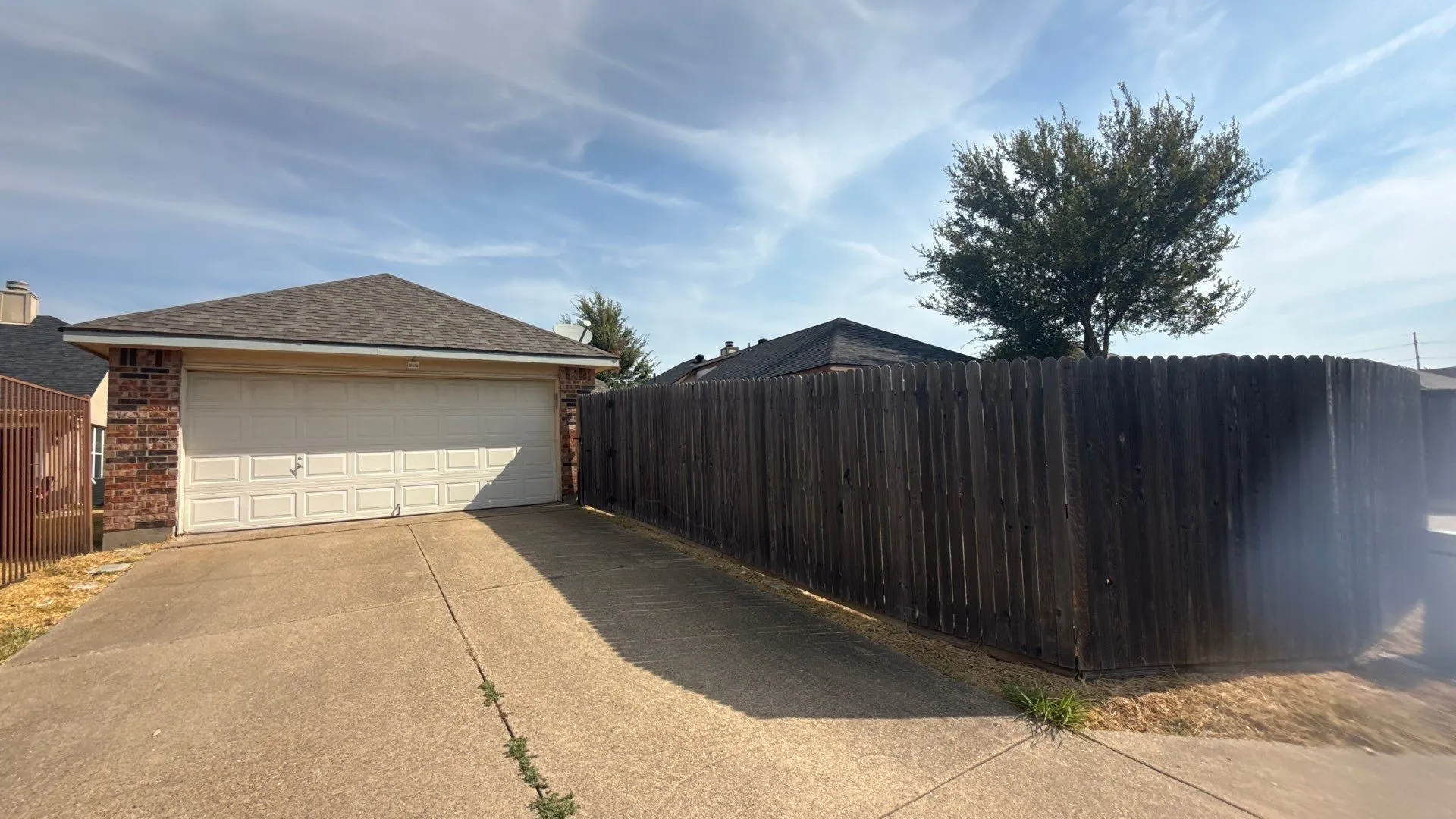 Attached two-car garage with a panel door, concrete driveway, brick exterior, and a wood privacy fence
