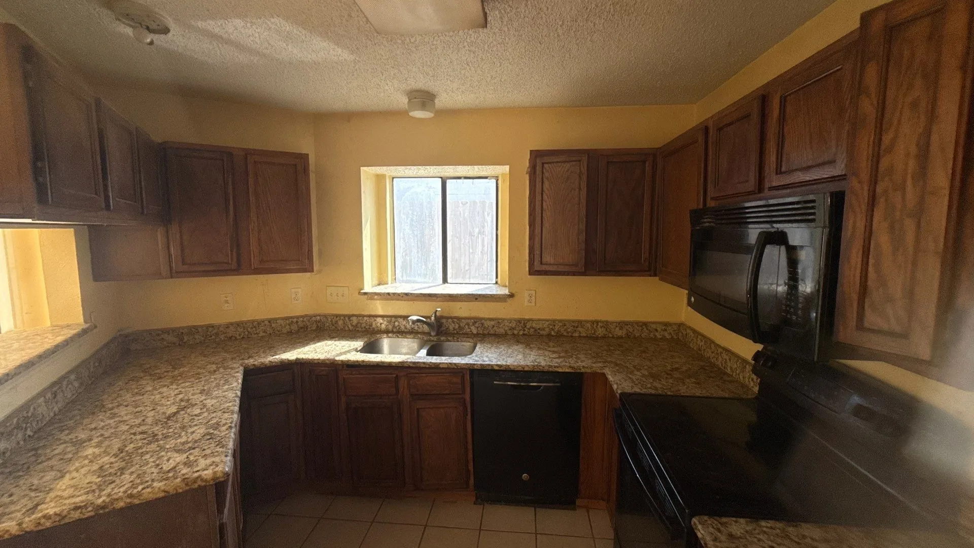 Kitchen featuring rich wood cabinetry, granite-finish countertops, and a full suite of black appliances, including a built-in microwave, dishwasher, and electric range