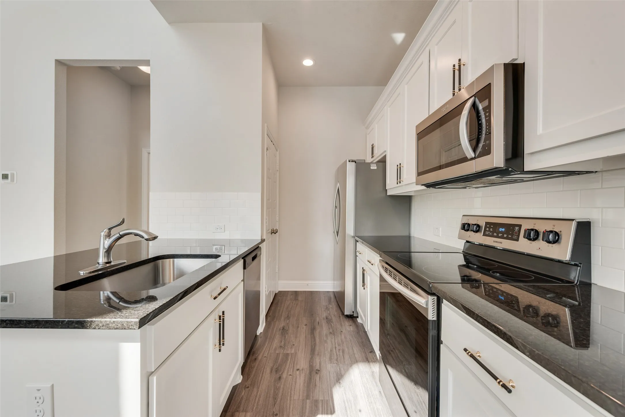 Galley kitchen featuring white cabinetry, dark countertops, stainless steel appliances, a subway tile backsplash, and wood-finish flooring