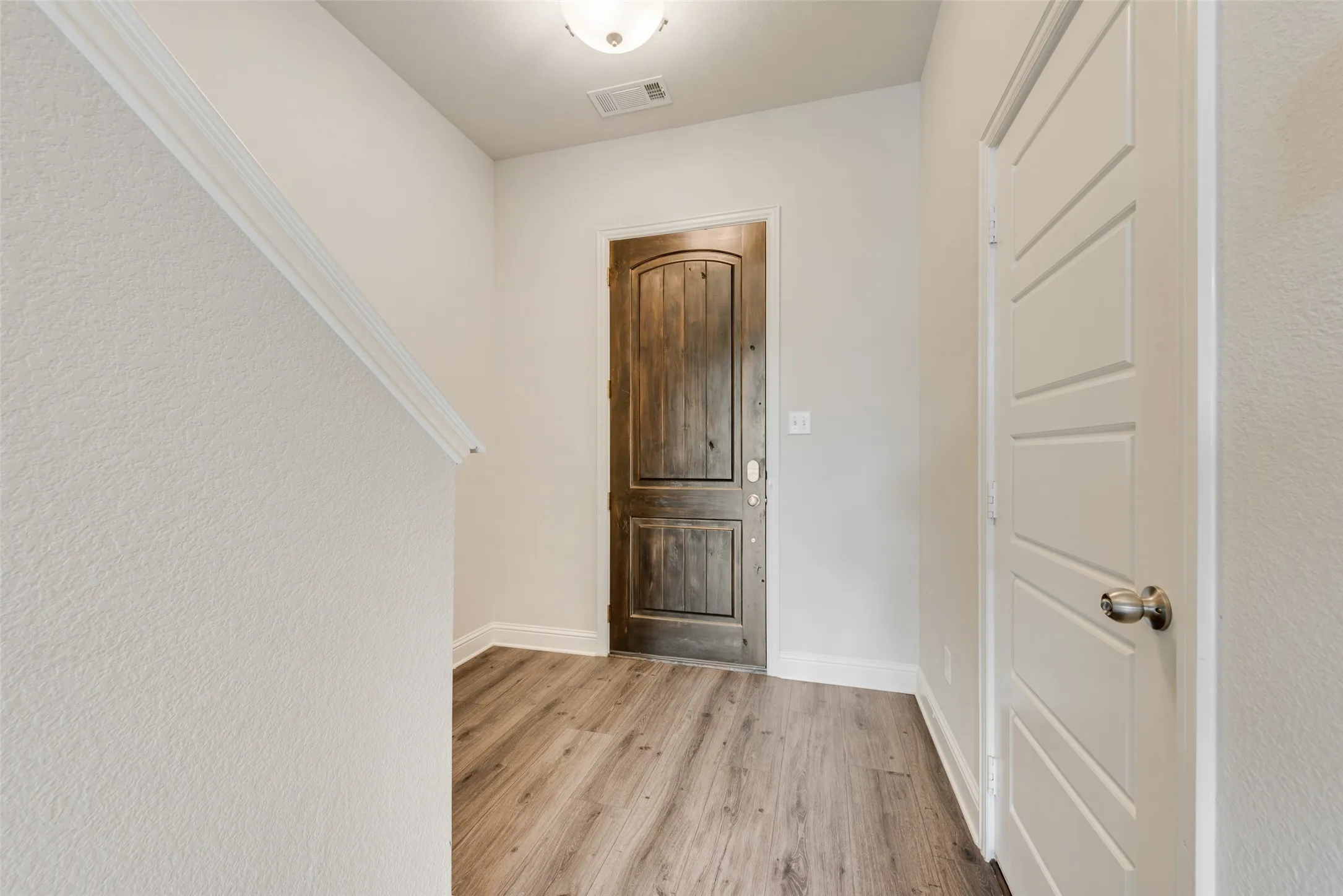 Wood-finish flooring, white trim, and a paneled white door