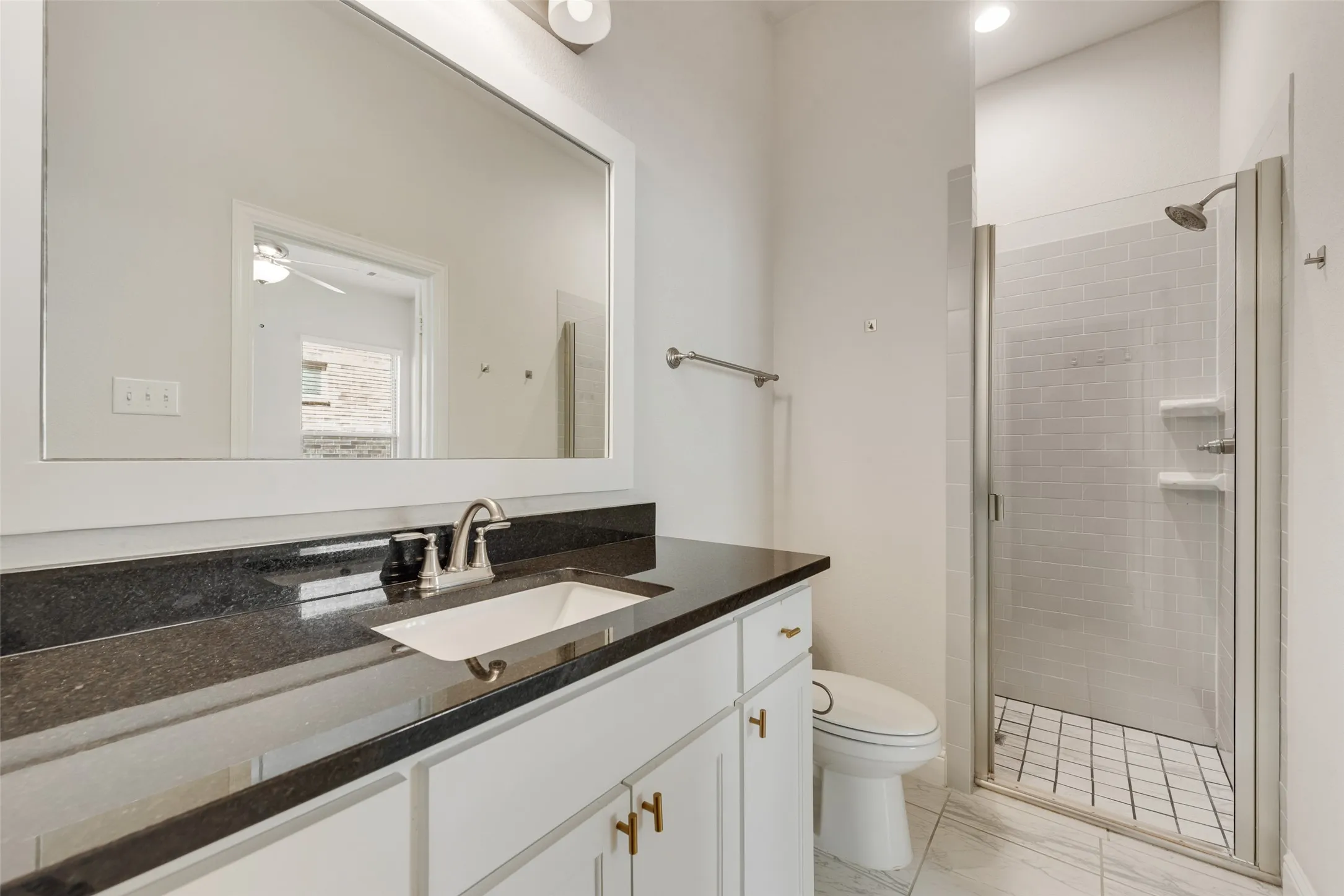 White vanity with gold-finish hardware, dark stone countertop, and integrated rectangular sink