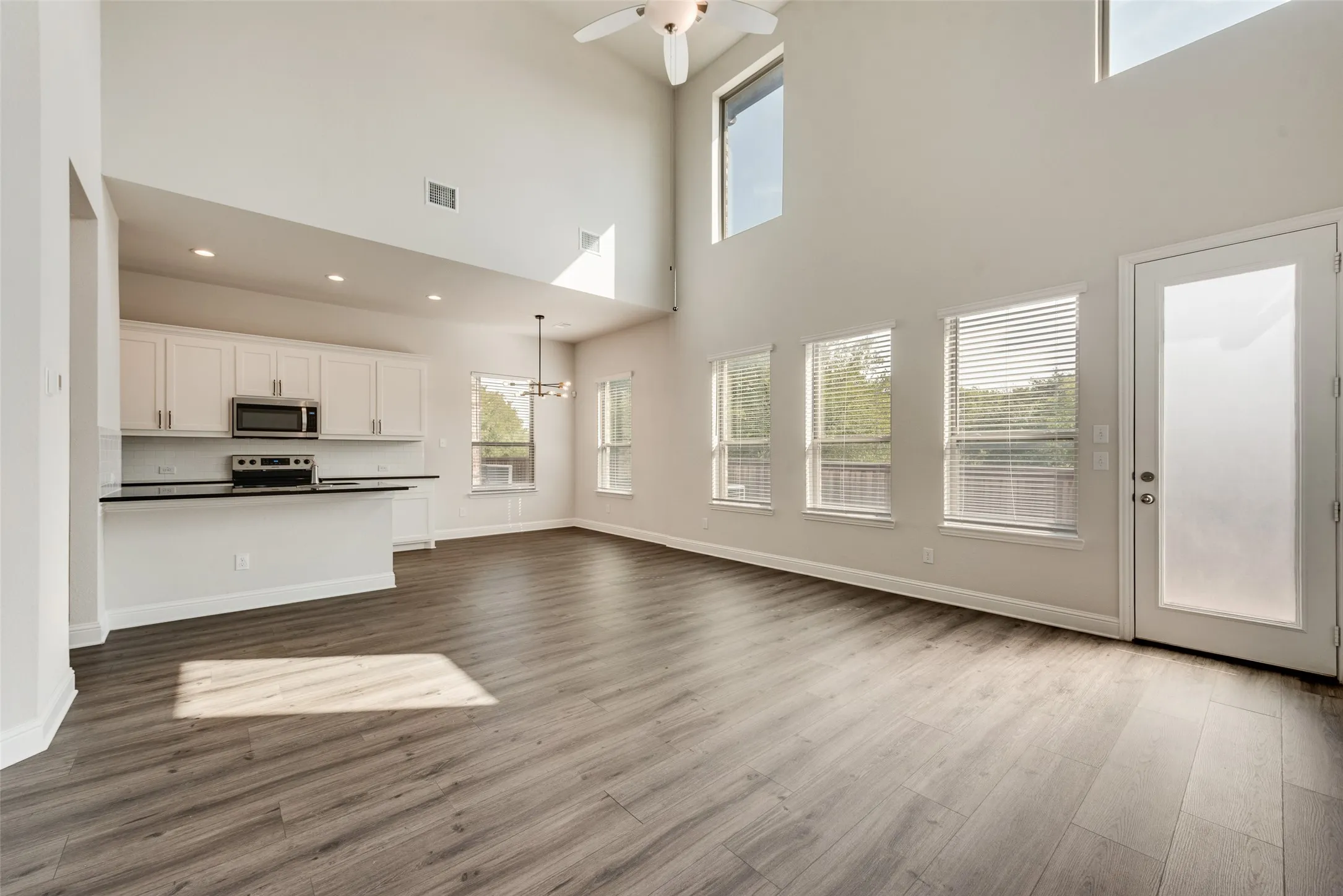 Vaulted ceilings, wood-finish flooring, white cabinetry, stainless steel appliances, and a ceiling fan