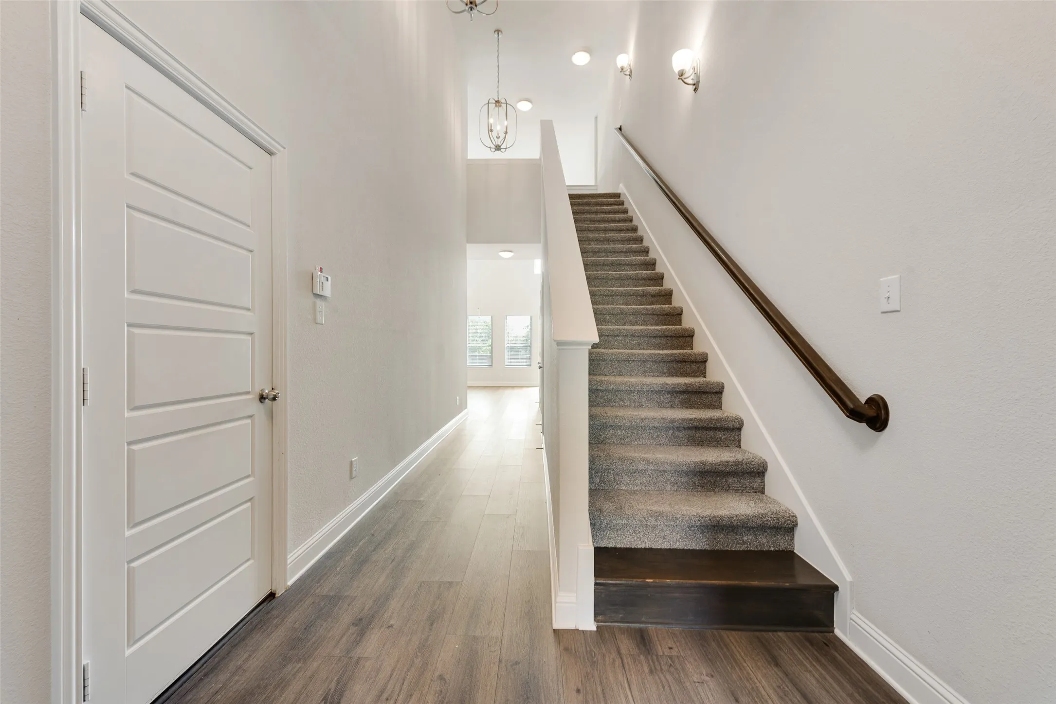 Wood-finish flooring, staircase with carpeting and dark wood treads, contemporary wall sconces, and a modern light fixture