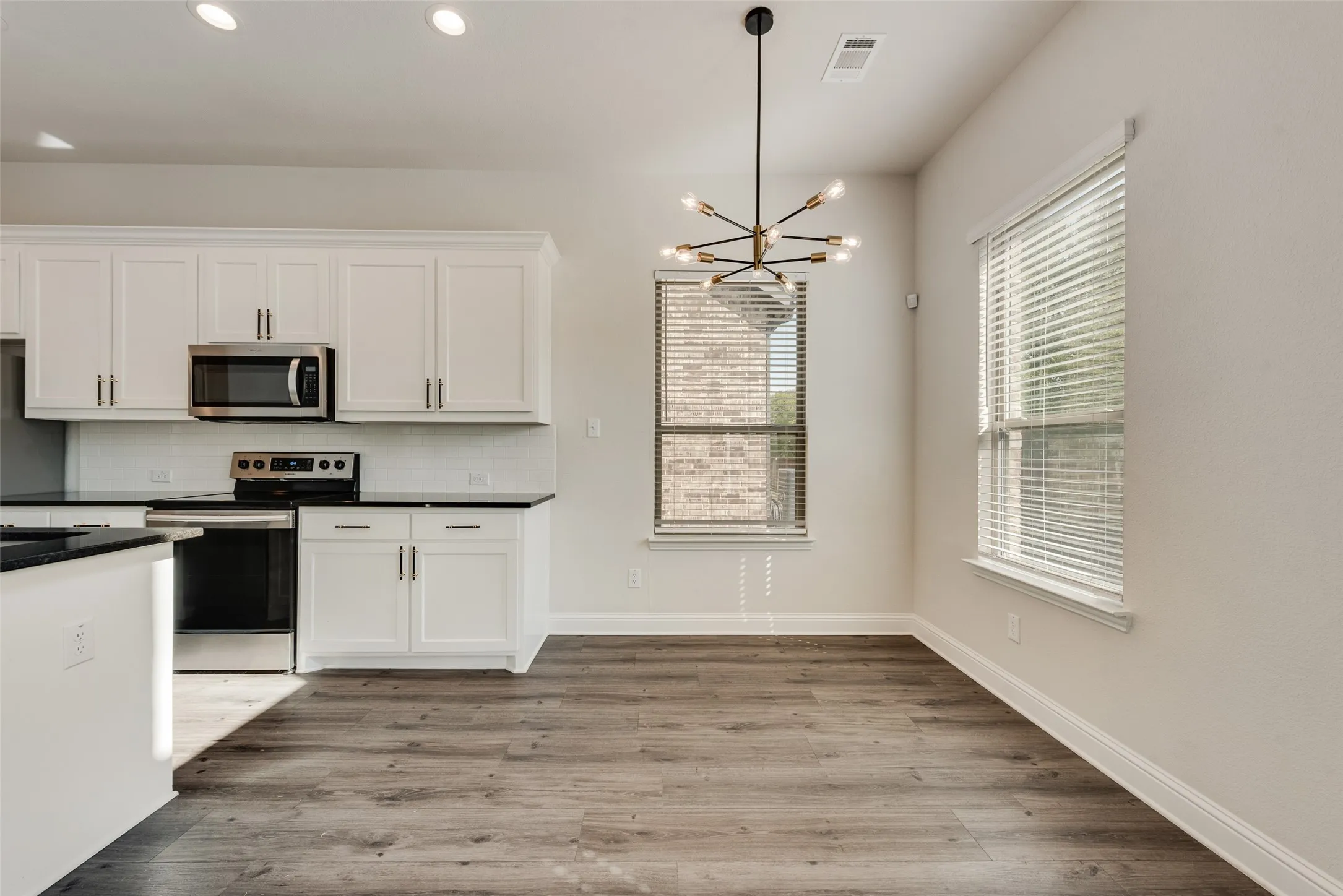 White cabinetry with sleek hardware, stainless steel appliances, dark countertops, wood-finish flooring, and a modern sputnik-style chandelier