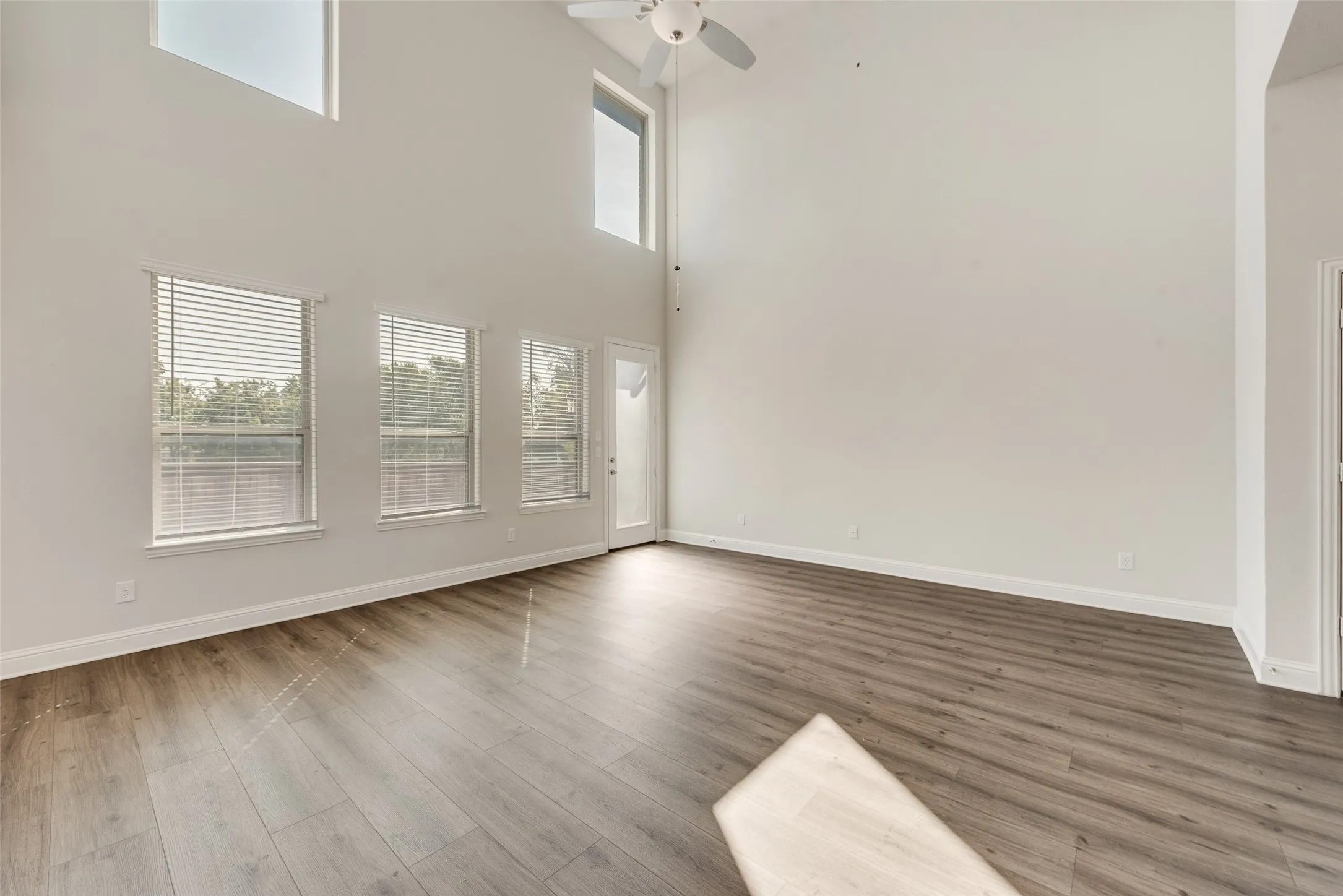 High ceilings, wood-finish flooring, multiple windows with blinds, transom windows, and a ceiling fan