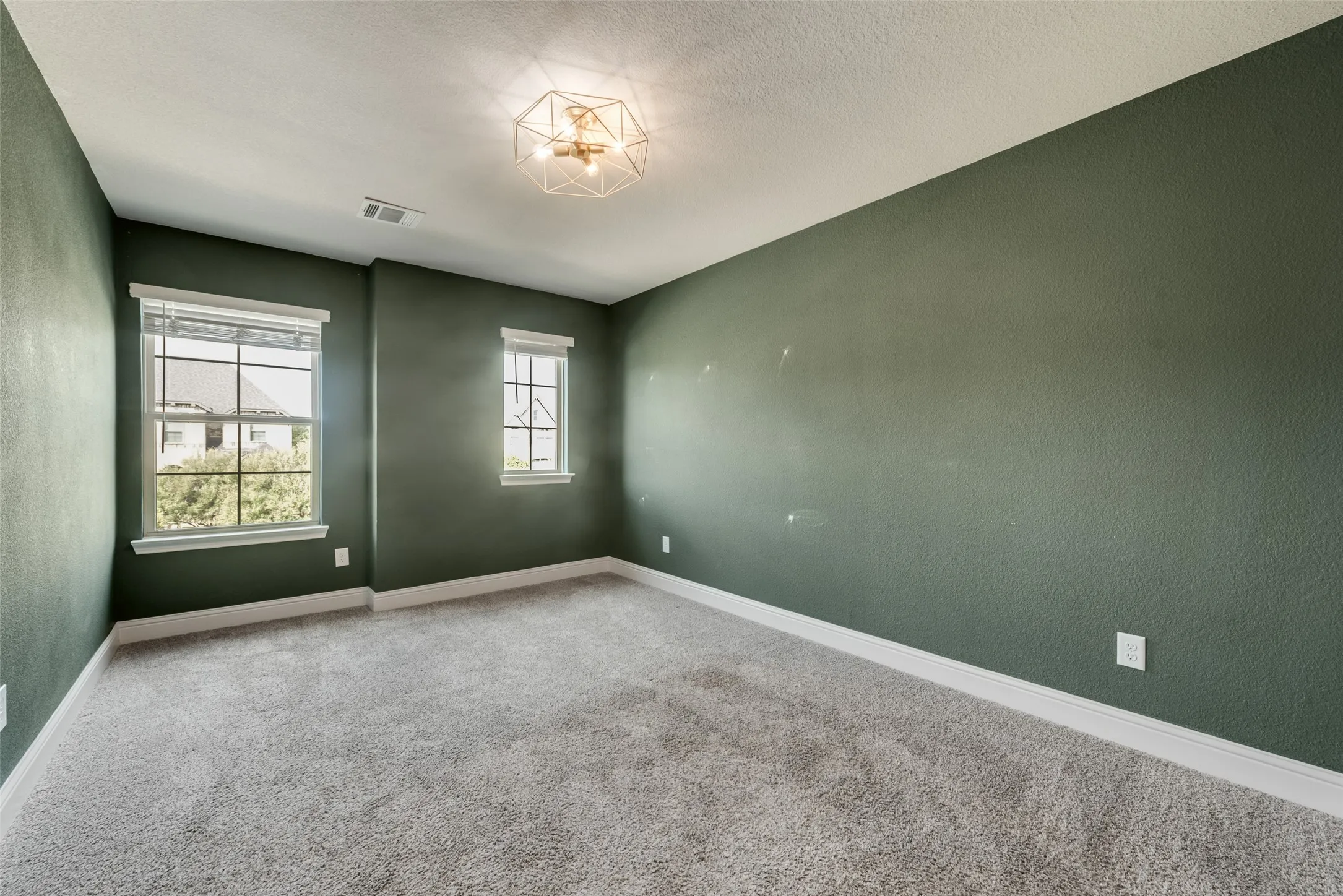 Carpeted flooring, two windows with blinds, and a decorative ceiling light fixture