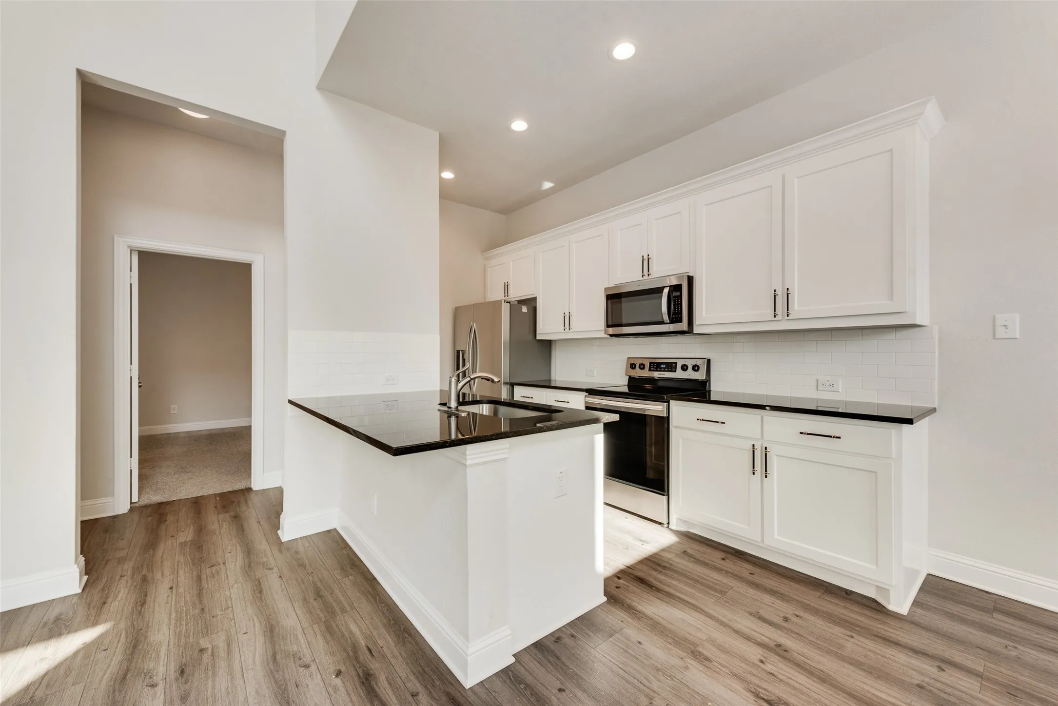 Kitchen featuring wood-finish flooring, white cabinetry, dark countertops, a white subway tile backsplash, and stainless steel appliances