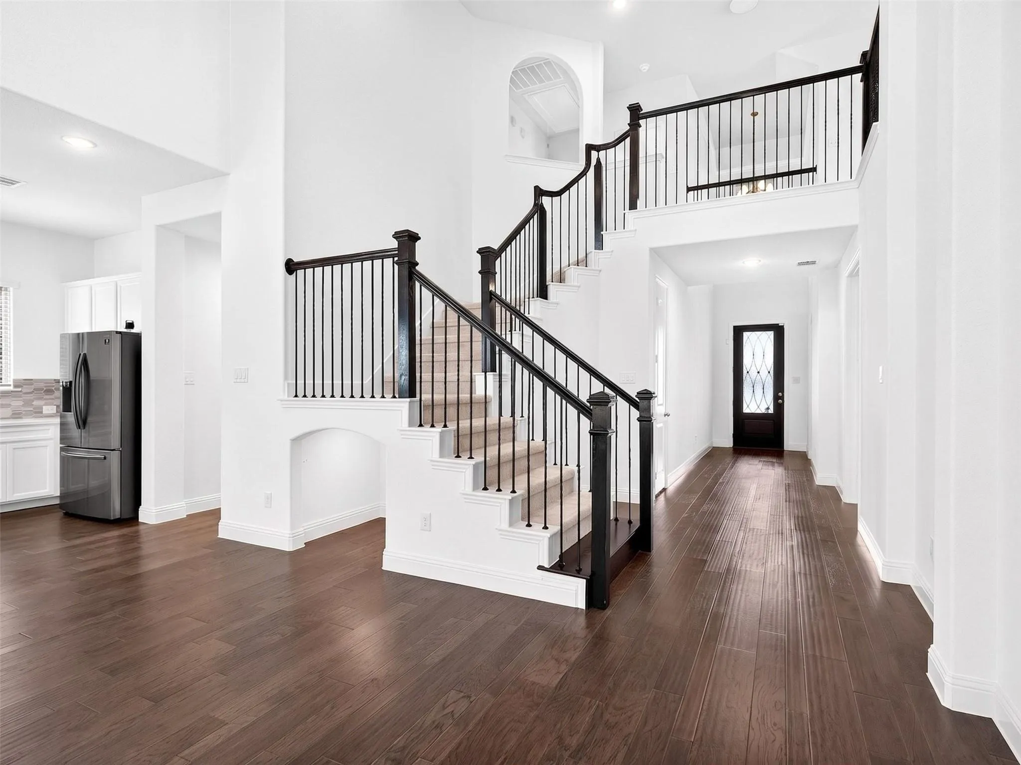 Expansive open concept interior featuring wood-finish flooring, a grand staircase with wrought iron balusters, a second-story landing, and a vaulted ceiling