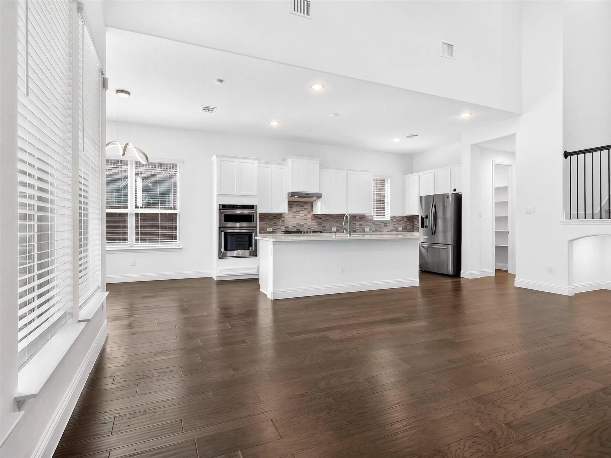 Open-concept living space featuring high ceilings, dark wood-finish flooring, and a kitchen with white cabinetry, stainless steel appliances, and a tiled backsplash