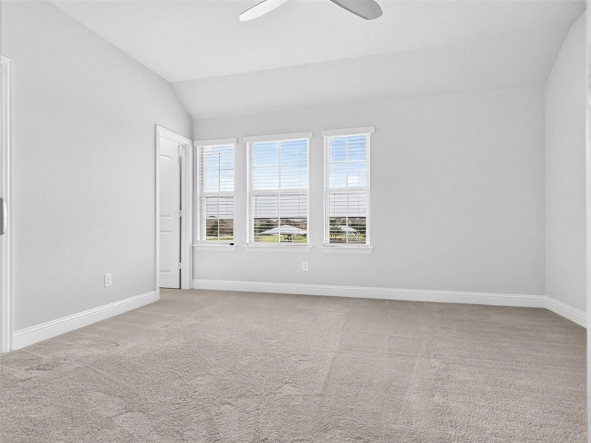 Vaulted ceiling, ceiling fan, triple windows, white trim, and light-toned carpeting
