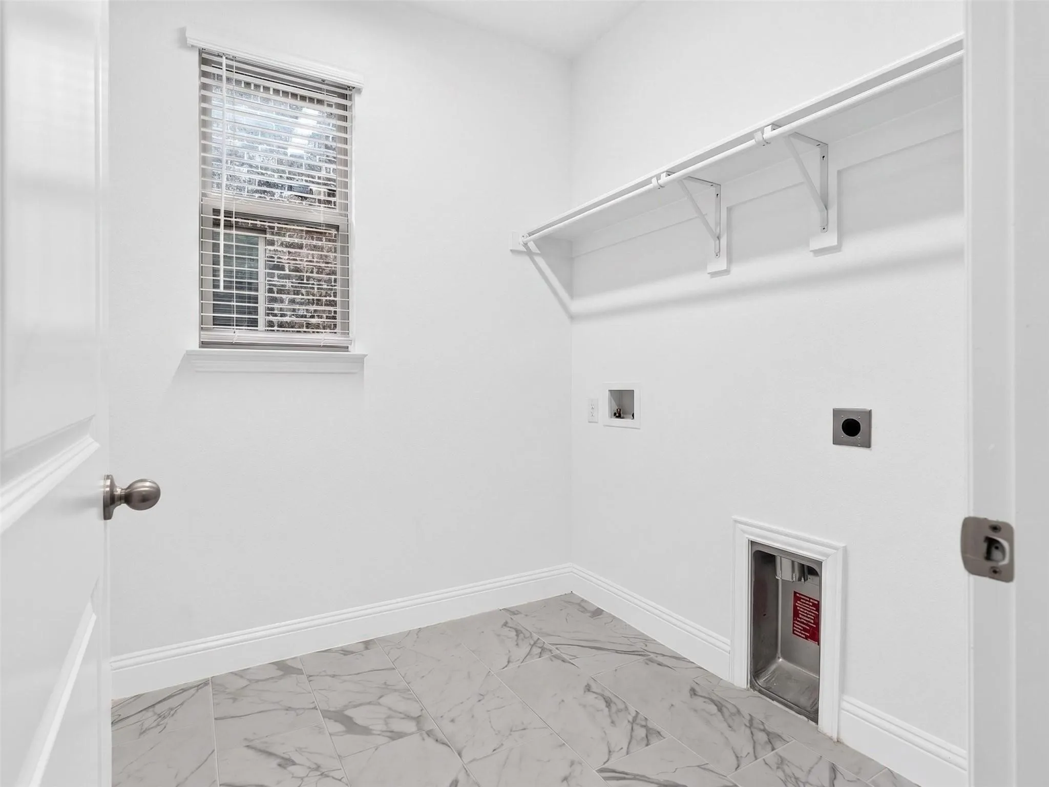 Laundry space with marble-look floor tile, window with blinds, and built-in shelving