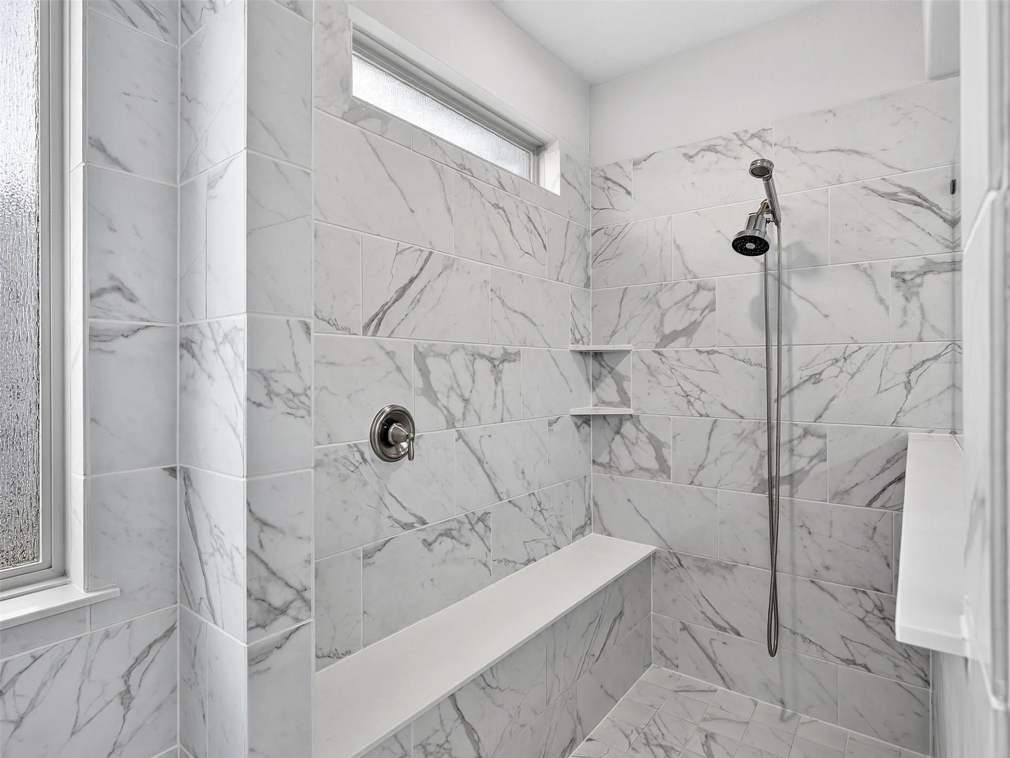 Walk-in shower with large format tile, built-in bench, dual shower heads, and an integrated shelf