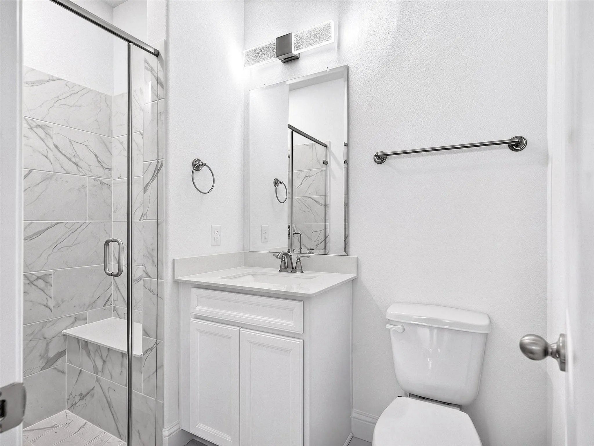 Glass-enclosed shower with a built-in bench and marble-look tile