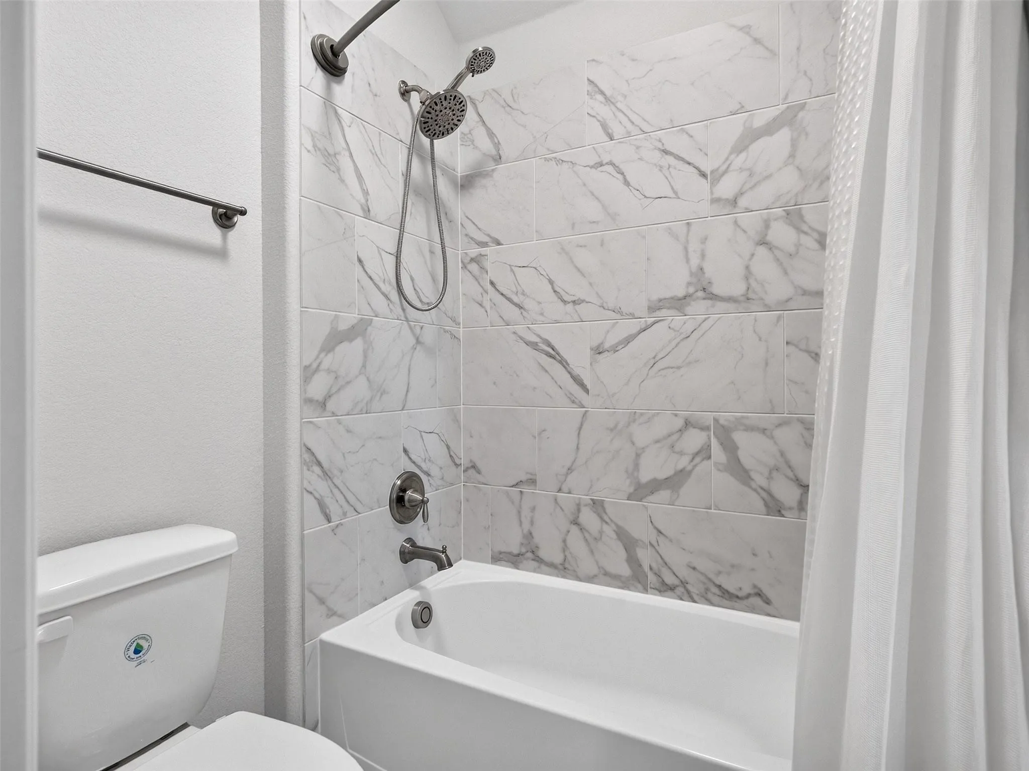 Bathtub and shower combination featuring a tiled surround with a marble-look finish and a brushed nickel shower fixture