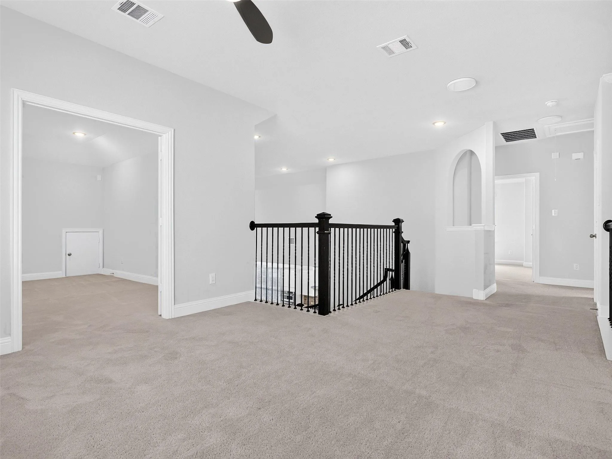 Open concept upper level featuring plush carpeting, a black wrought iron staircase railing, recessed lighting, and an arched hallway opening
