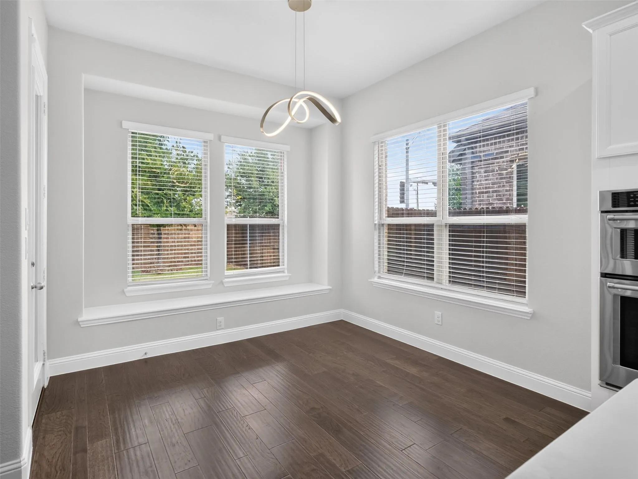 Recessed window area with three large windows, modern chandelier, wood-finish flooring, and crisp white trim