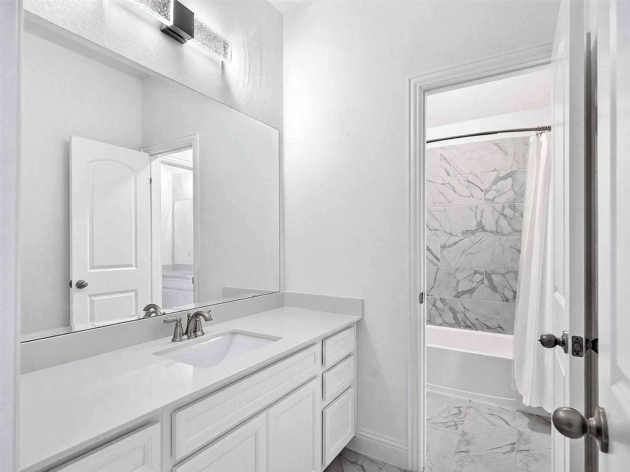 White vanity with a built-in sink and brushed nickel faucet, large wall mirror, and modern vanity lighting