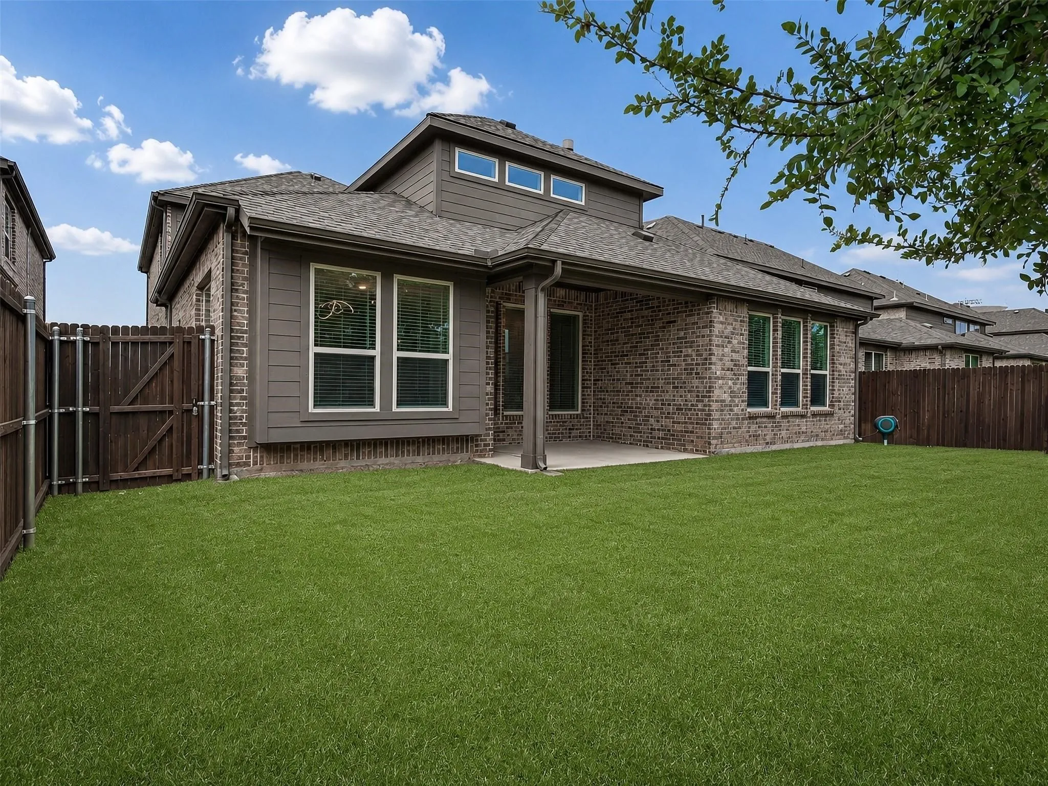 Expansive green lawn, covered patio, brick and siding exterior, multi-pane windows, and privacy fencing